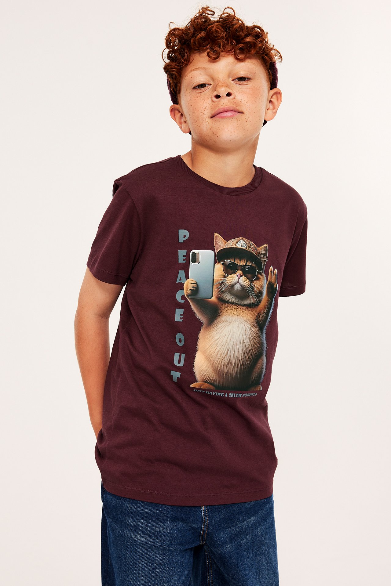 Ung pojke i mörkröd t-shirt med tryck av katt med solglasögon, helsida frontvy.