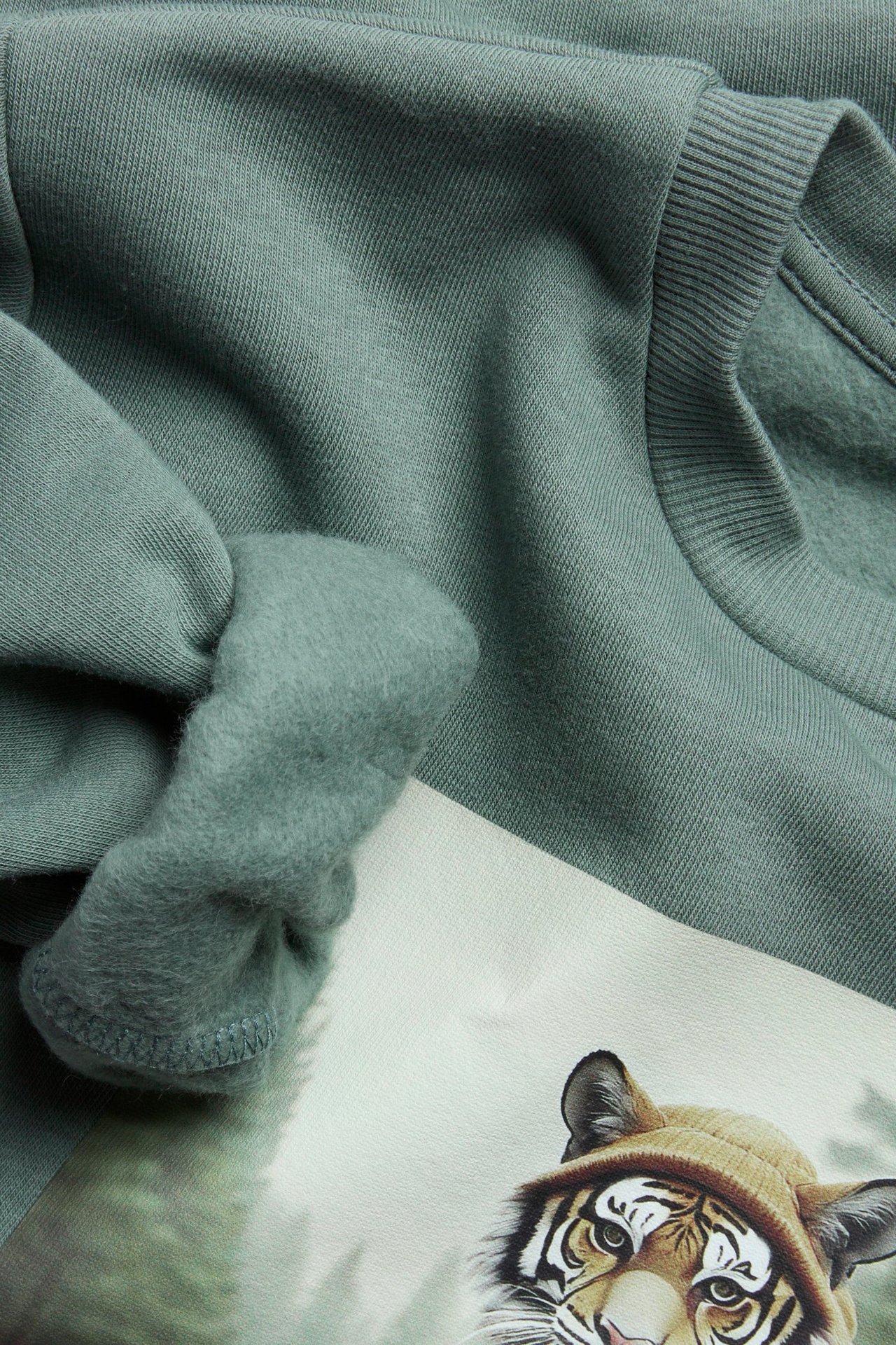 Zbliżenie na khaki zieloną bluzę z bawełny, z czesanym wnętrzem i dużym nadrukiem tygrysa.