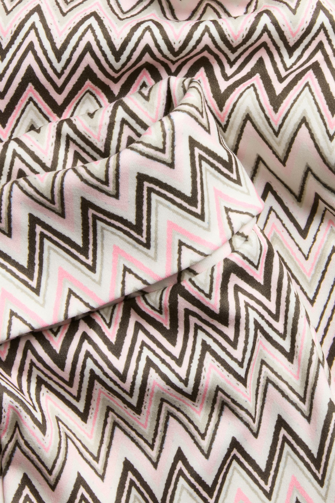 Zbliżenie na wzorzysty beżowy materiał z zygzakowatym wzorem w brązie, jasnej szarości, różu i bieli.