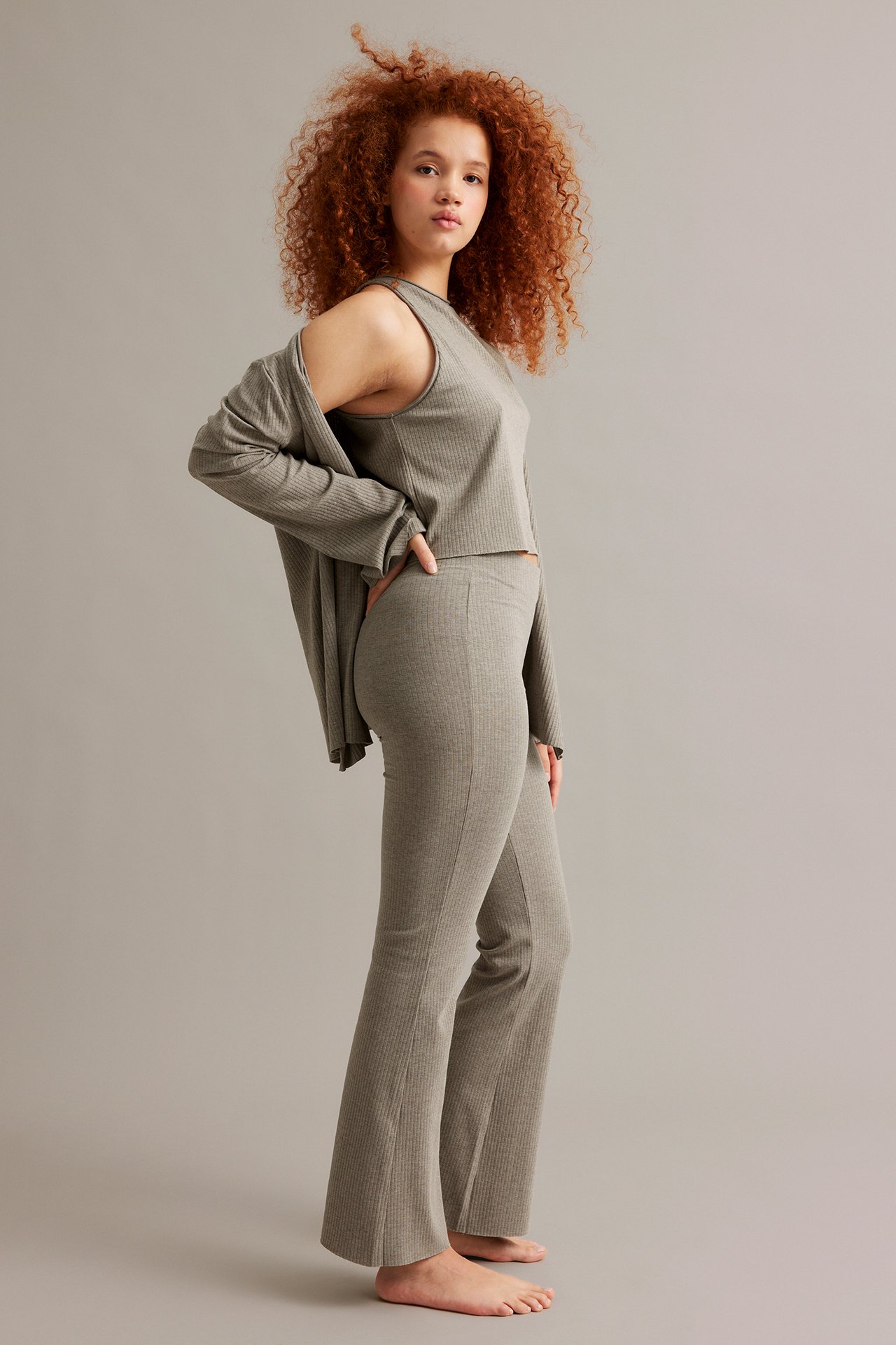 Naisen sivukuva meleratuissa ruskeissa ribbineulotuissa bootcut-housuissa, yhteensopivassa topissa ja avoimessa neuletakissa.