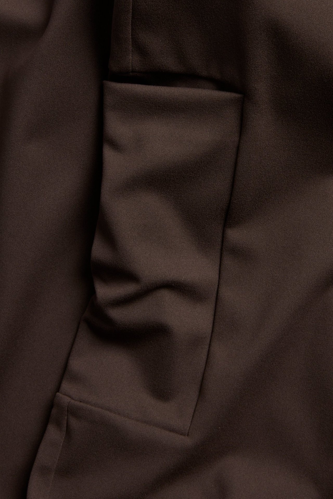 Zbliżenie na ciemnobrązowe legginsy treningowe bootcut z boczną kieszenią na nogawce, z miękkiego, elastycznego materiału.