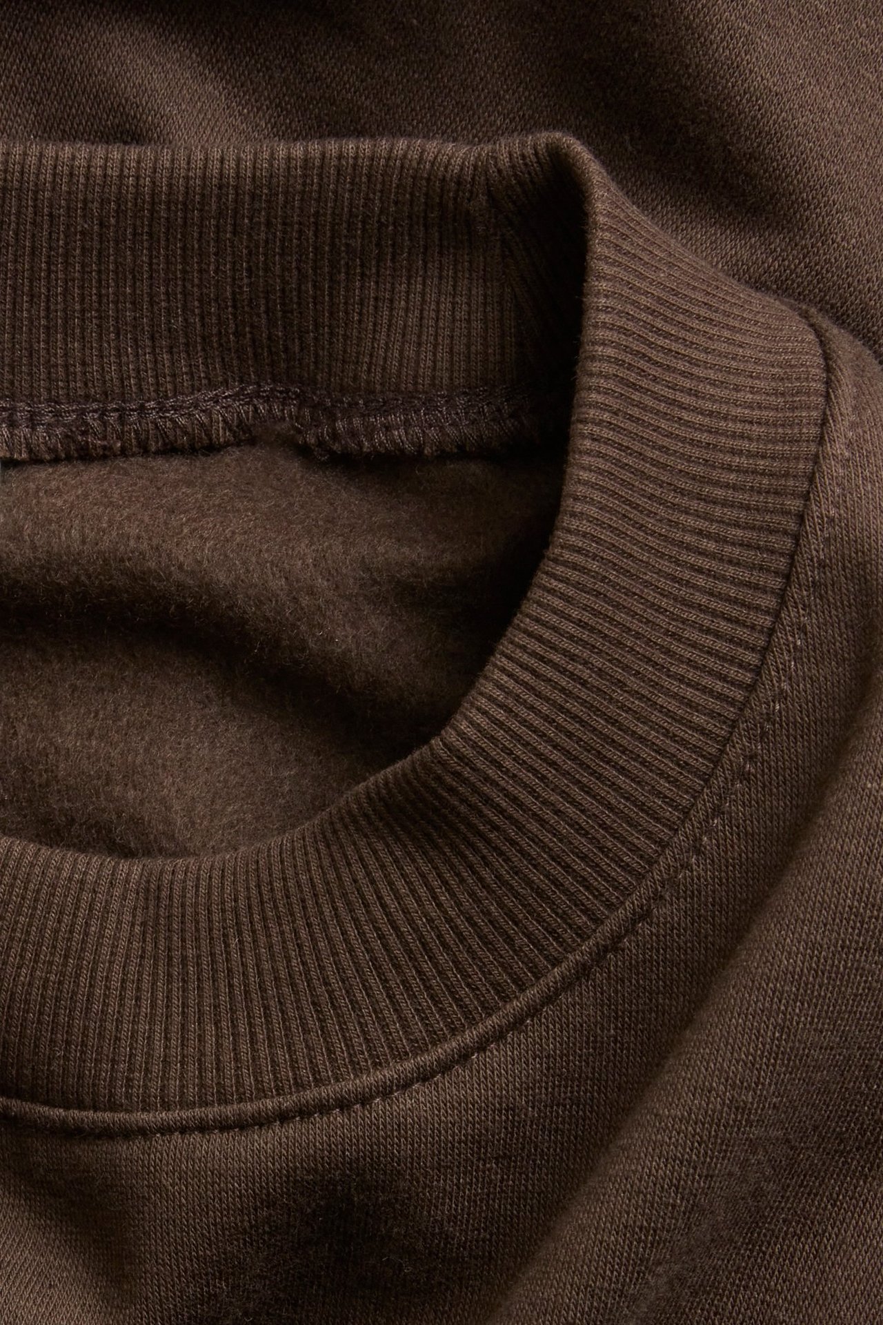 Zbliżenie na ciemnobrązową bluzę z prążkowanym kołnierzem i miękkim, szczotkowanym wnętrzem.