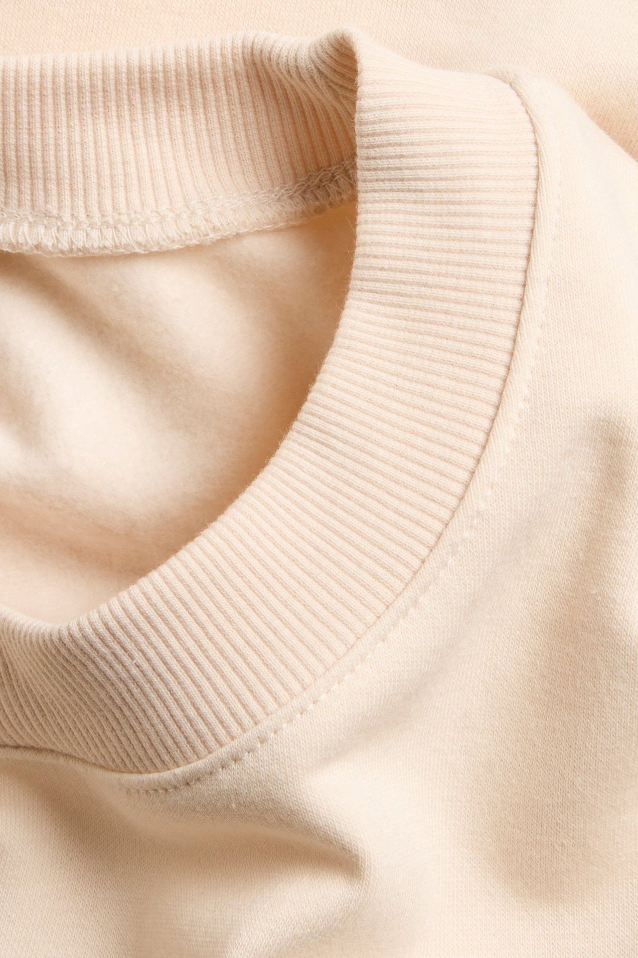 Zbliżenie prążkowanego okrągłego dekoltu jasnobeżowej, krótkiej bluzy.