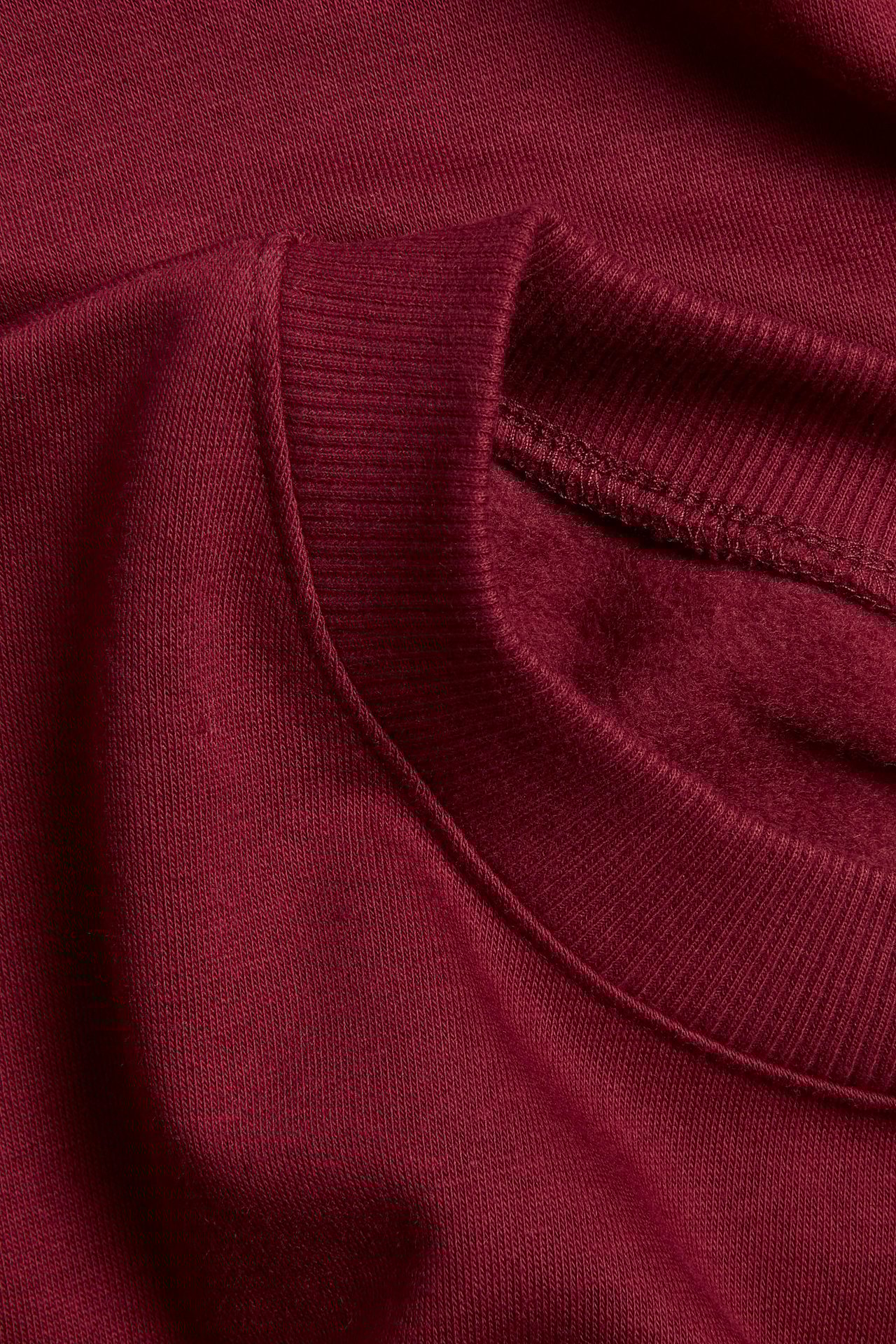Zbliżenie na ciemnoczerwoną, jednolitą bluzę z okrągłym, prążkowanym dekoltem i szczotkowanym wnętrzem z polaru.