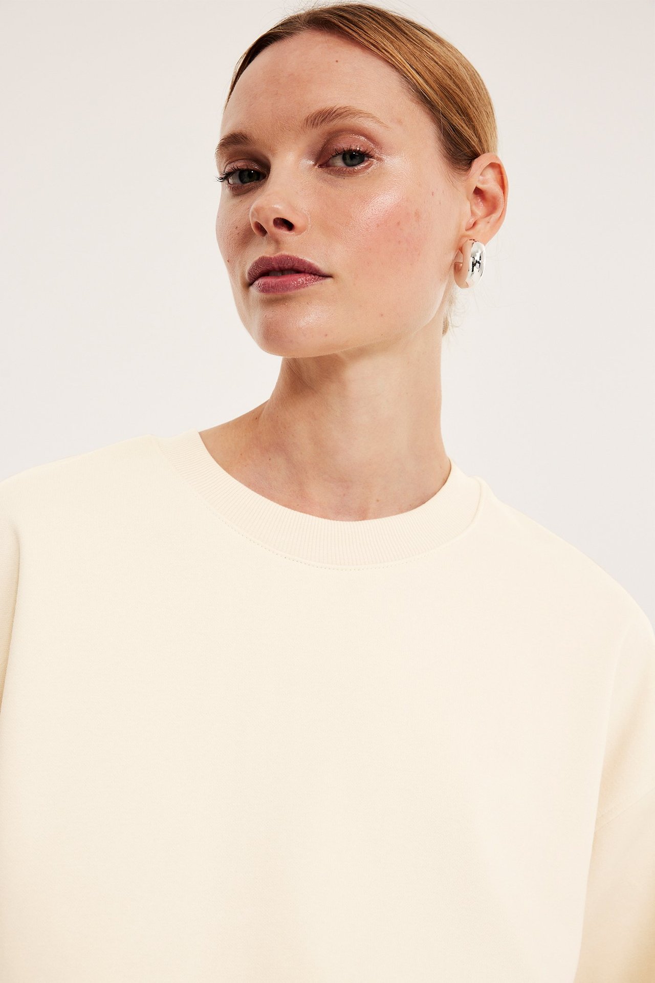 Zbliżenie na kobietę w gładkiej, kremowej, krótko rękawowej bluzie i srebrnych kolczykach kołach.