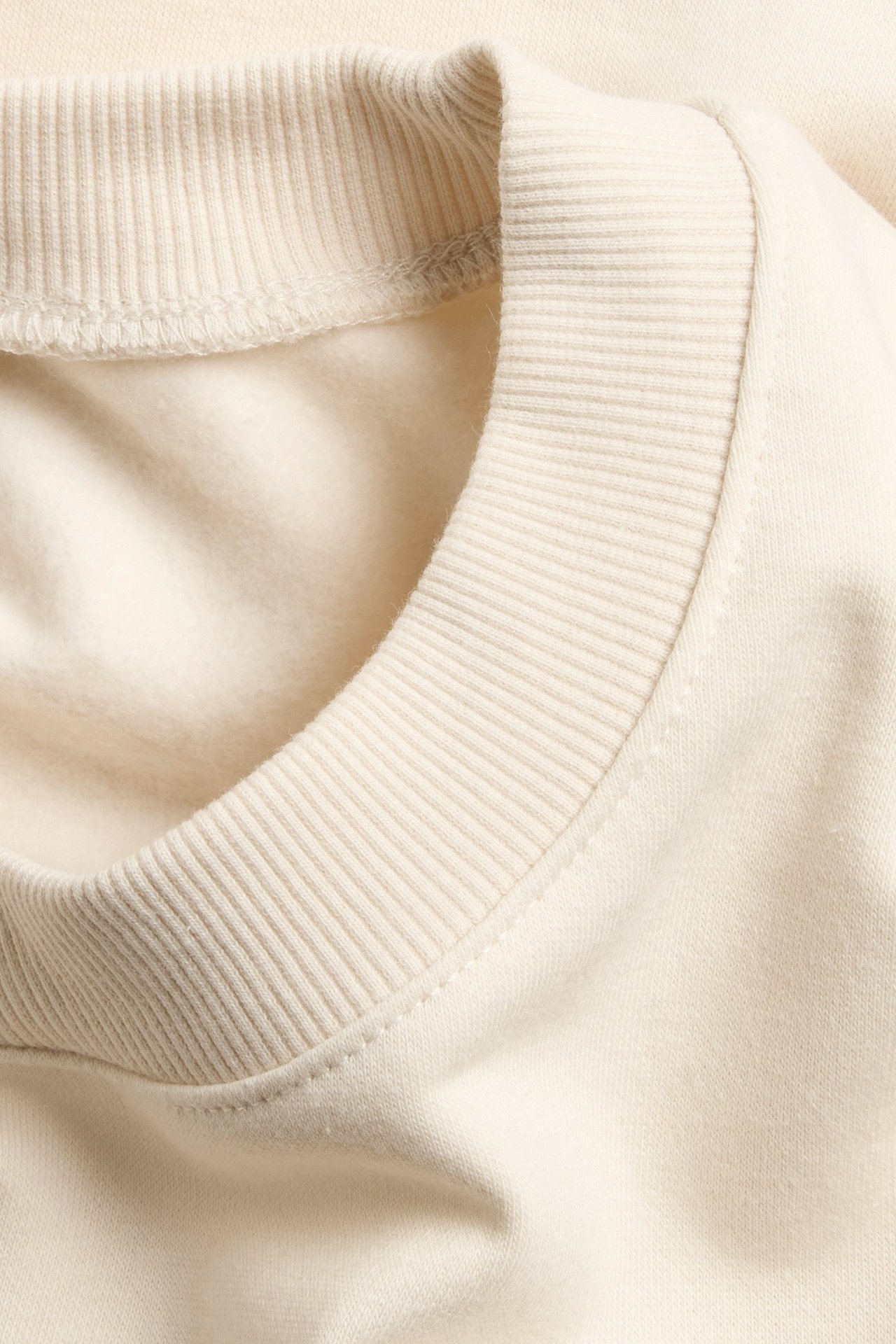 Zbliżenie na kremową, krótko rękawową bluzę z prążkowanym okrągłym dekoltem.