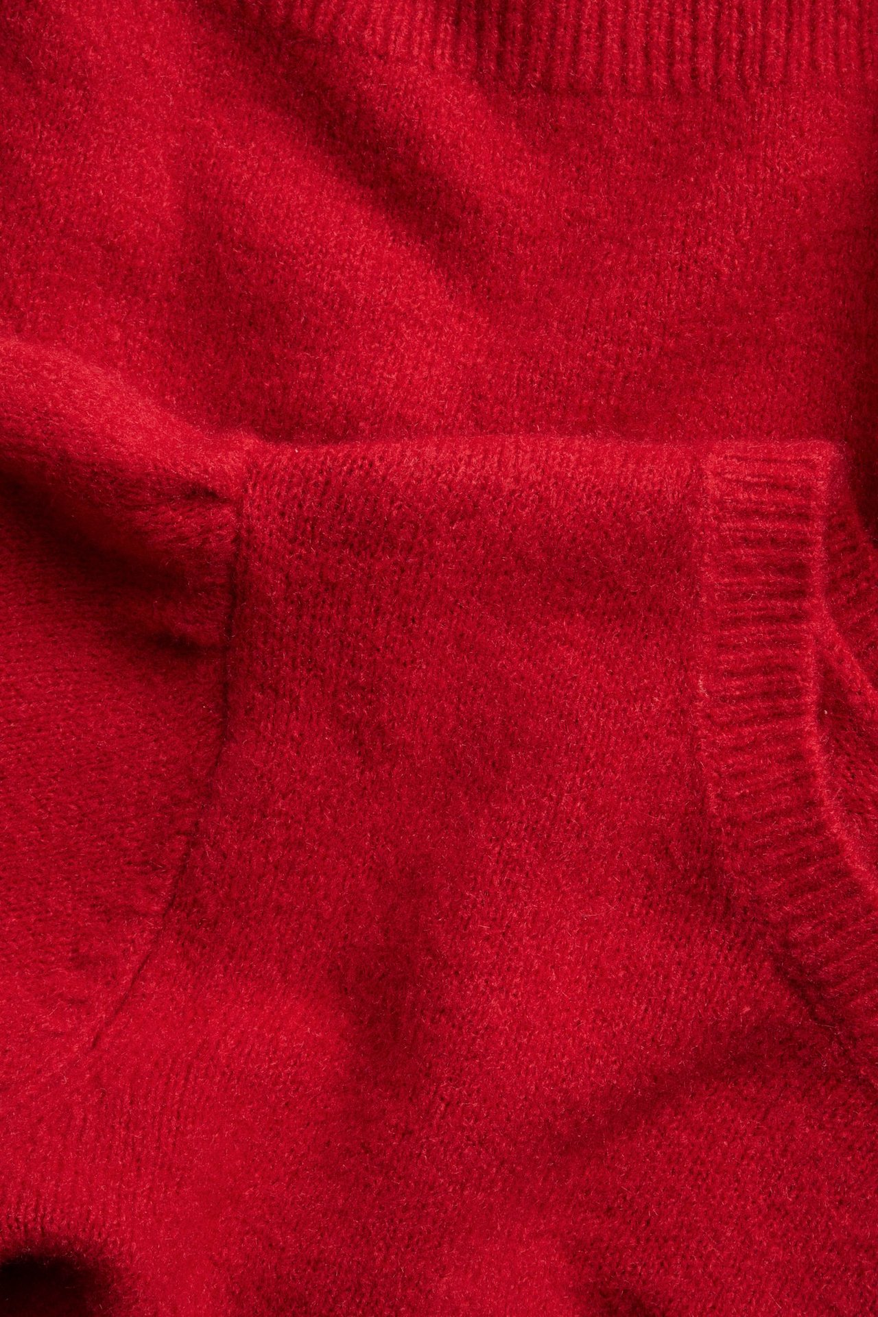 Zbliżenie czerwonego swetra z dzianiny z detalem bufiastych rękawów i widocznym ściągaczem.