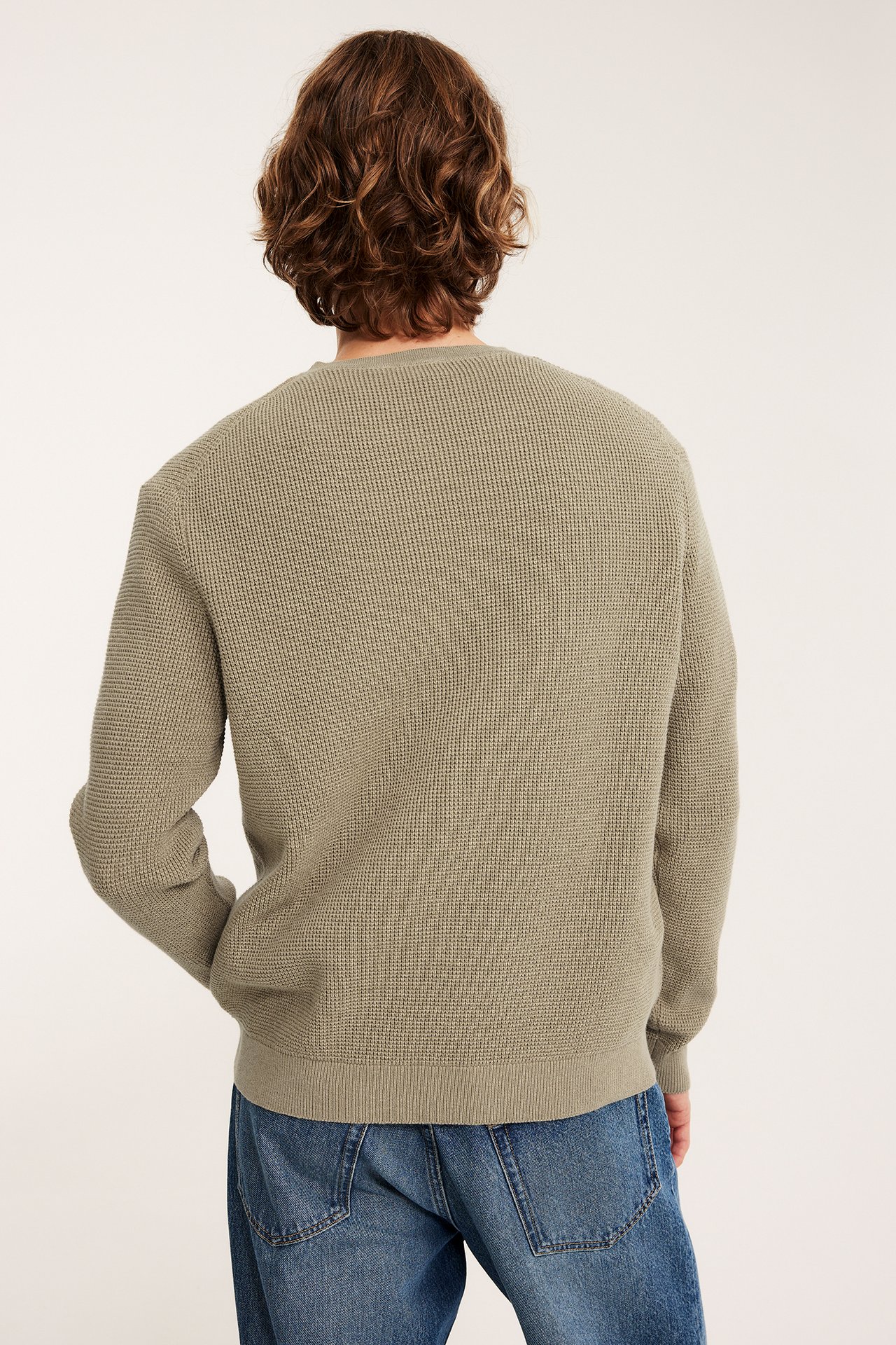 Mies selin, yllään beigemelange neulepusero ja siniset farkut.