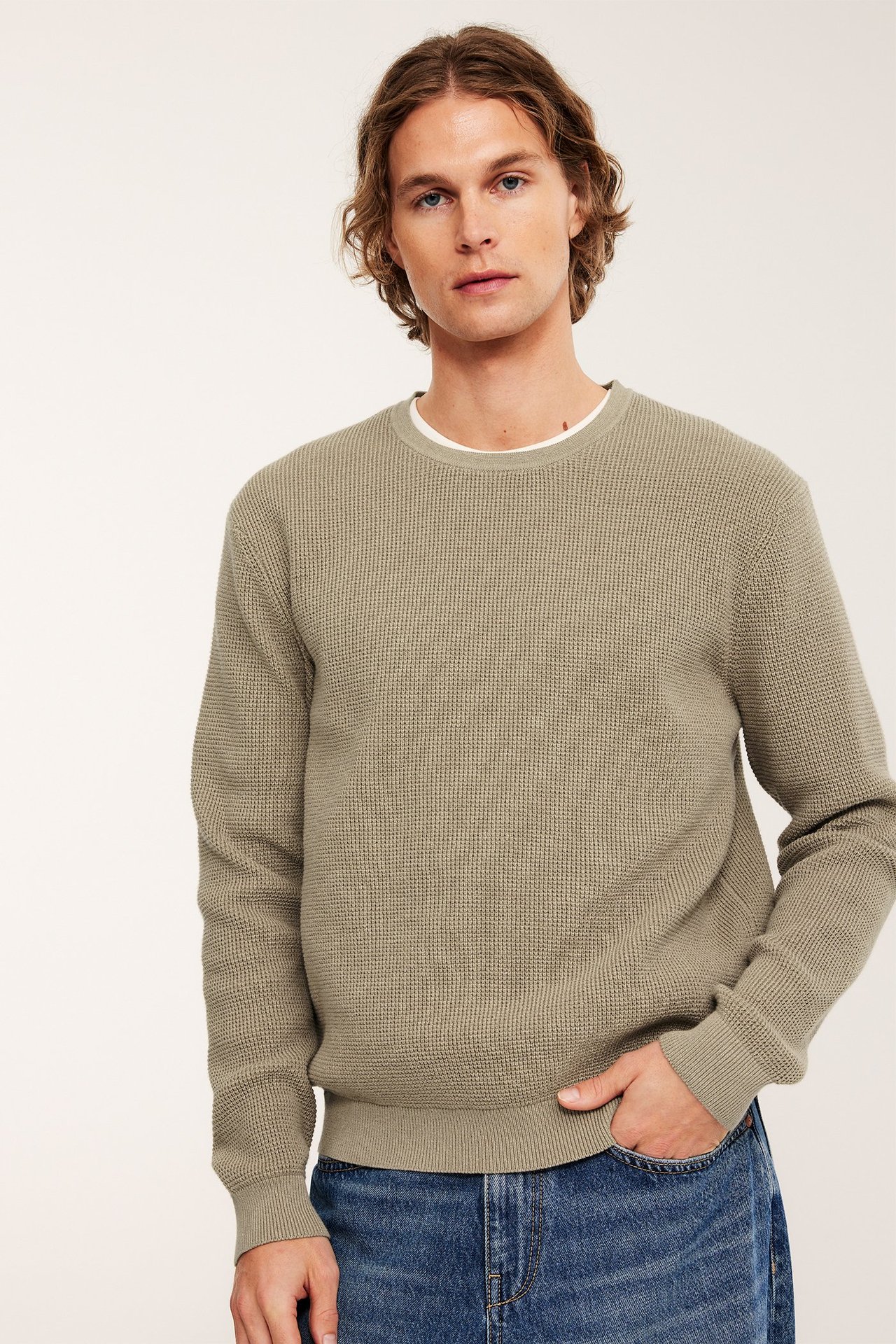 Forsidebilde, mann i beige melert strikkegenser over hvit t-skjorte, med blå jeans.