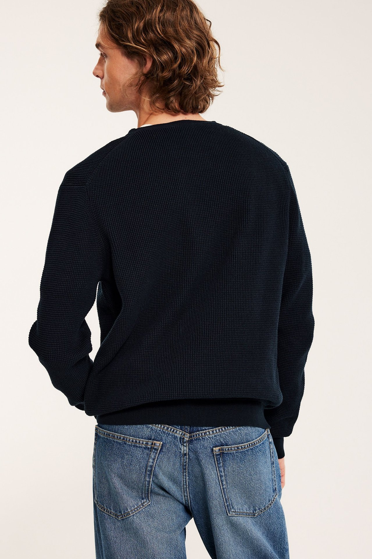 Mies takaa-oikealta: tummansininen yksivärinen neulepusero ja vaaleansiniset farkut.