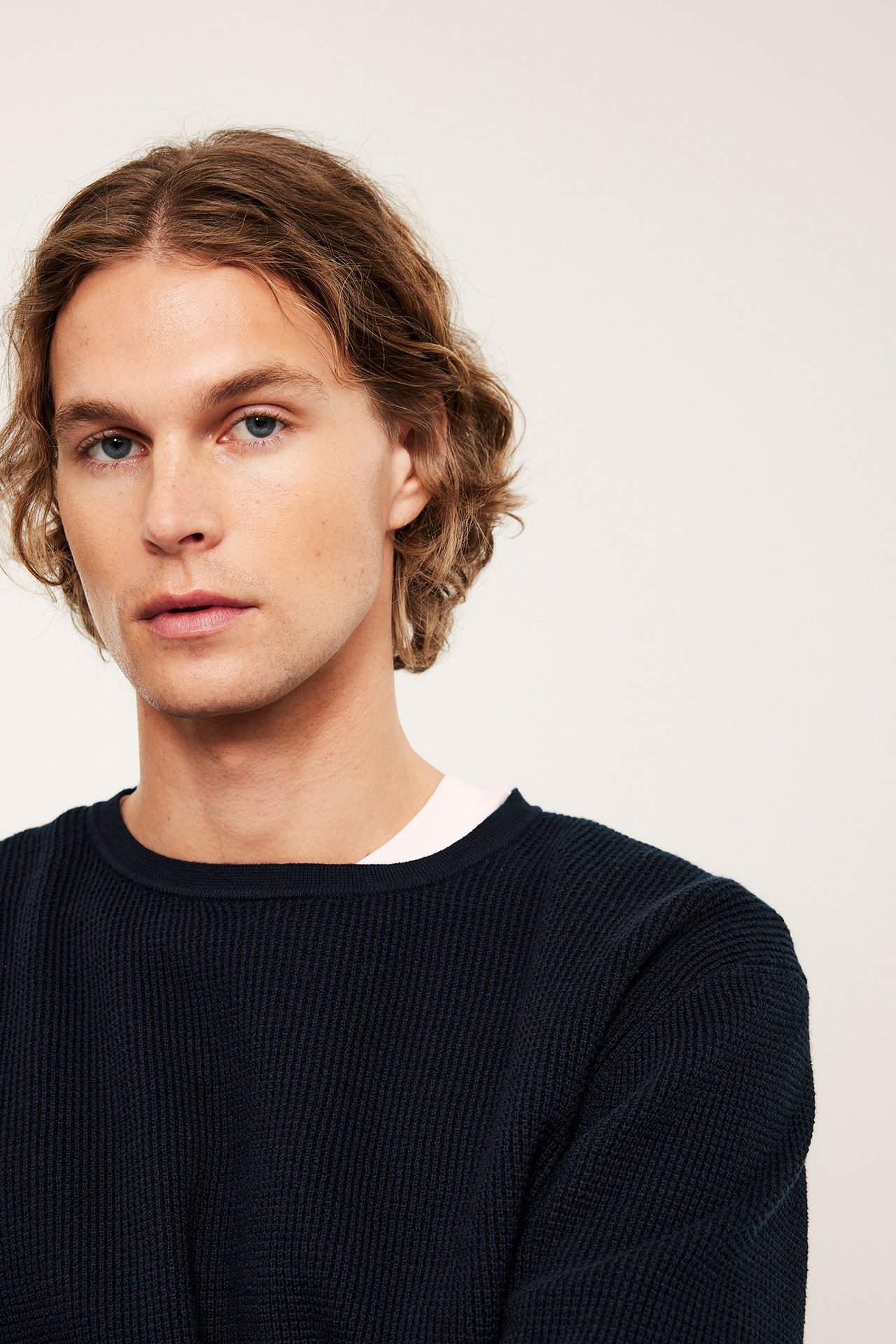 Edestäpäin: mies yllään tummansininen yksivärinen neulepusero valkoisen t-paidan päällä.