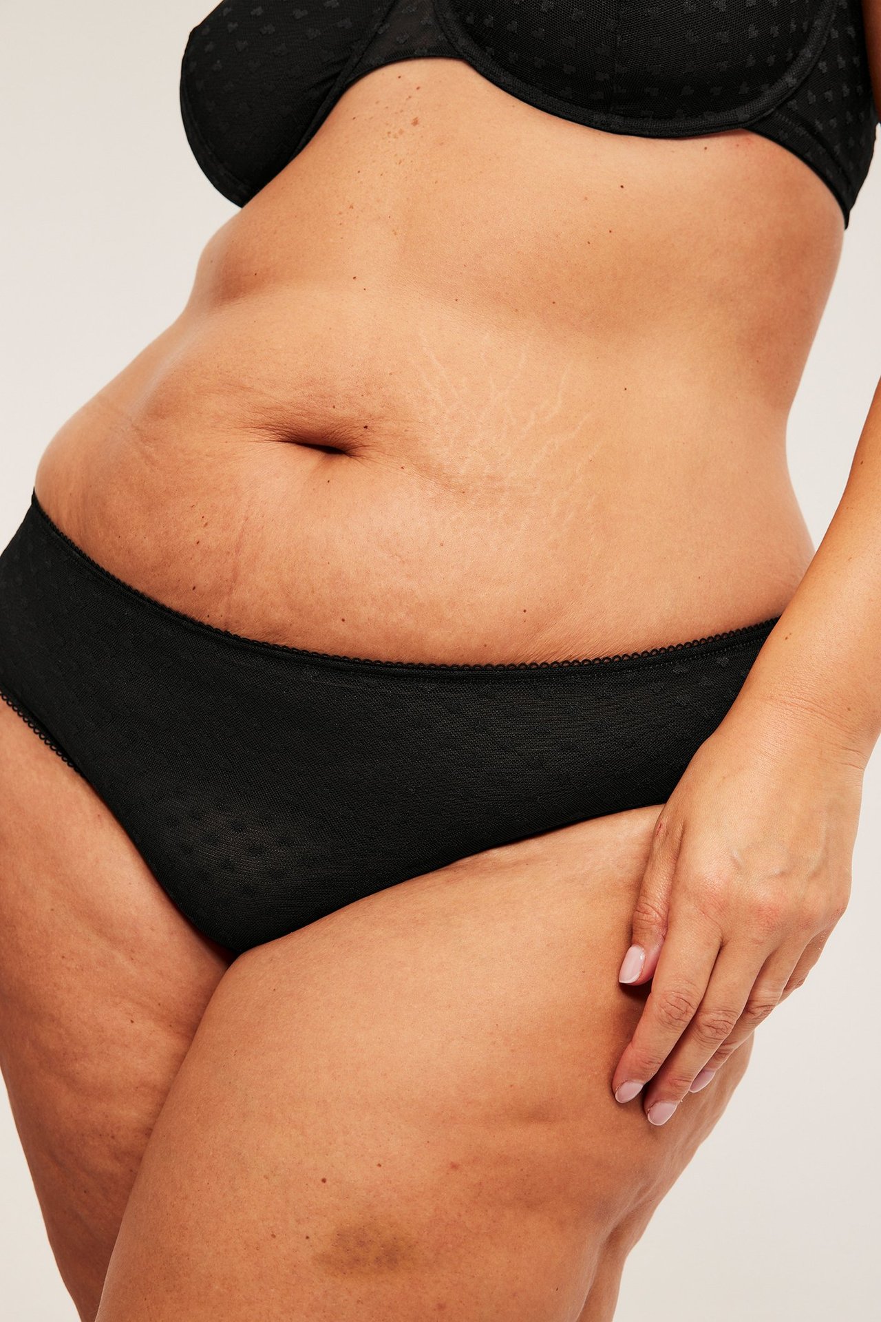 Nærbilde av kvinne i svart mesh-truse med hjertemønster, picotkant og svart mønstret BH.