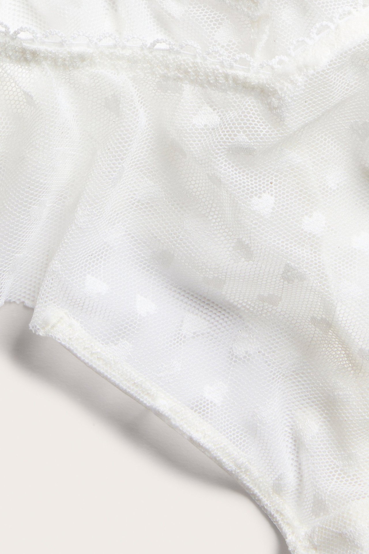 Närbild av offwhite spetsstring med delikata hjärtmönster och picotkant.