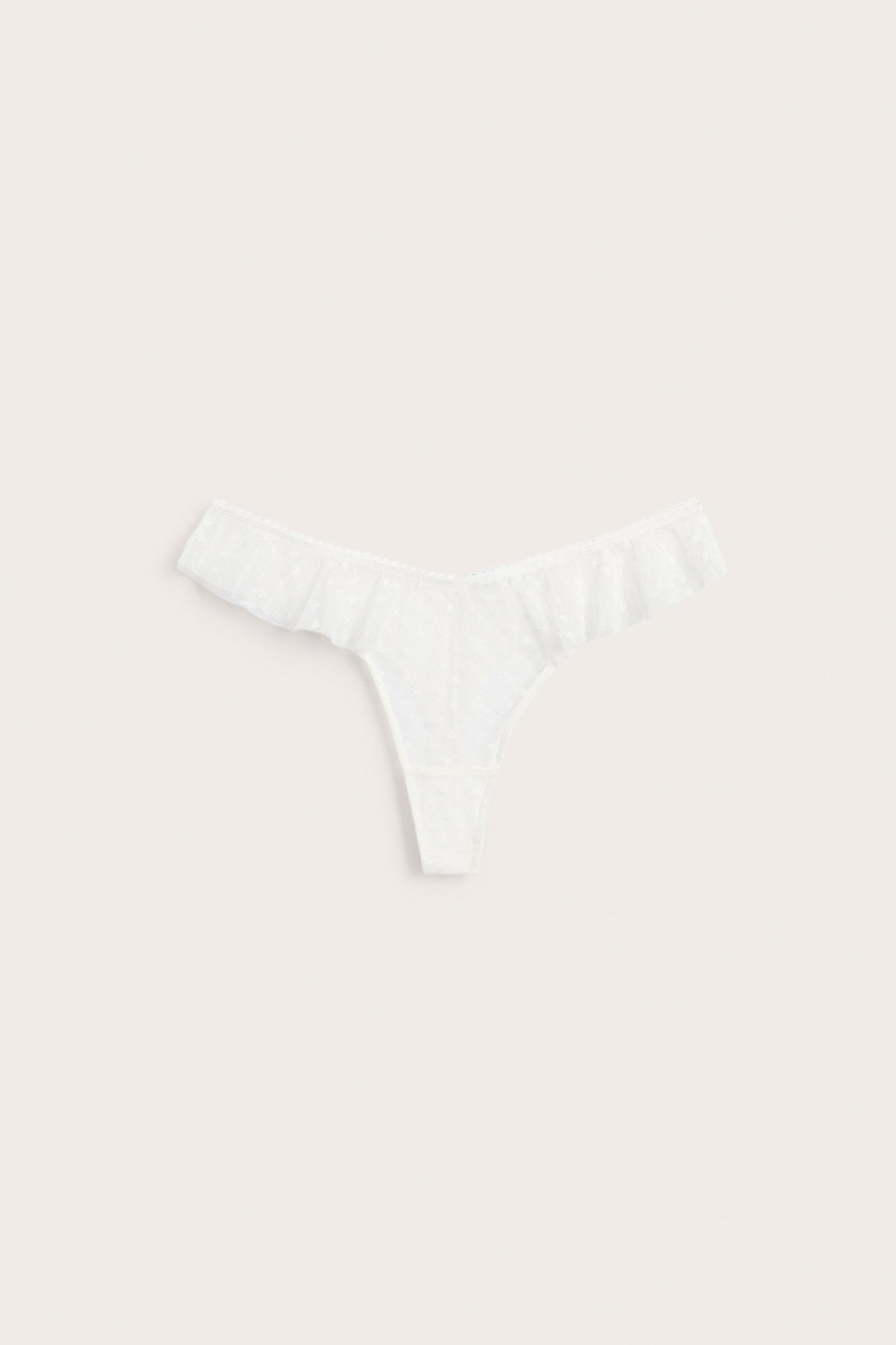 Ovanifrån: En offwhite spets-halfstringtrosa med V-formad midja och volanger längs benöppningarna.