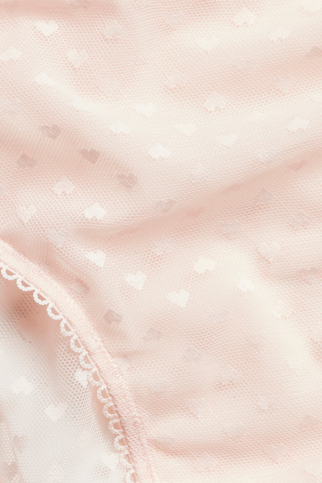 Nærbilde av lys rosa hjerte-mønstrede brazilian truser med hvit picot-kant.