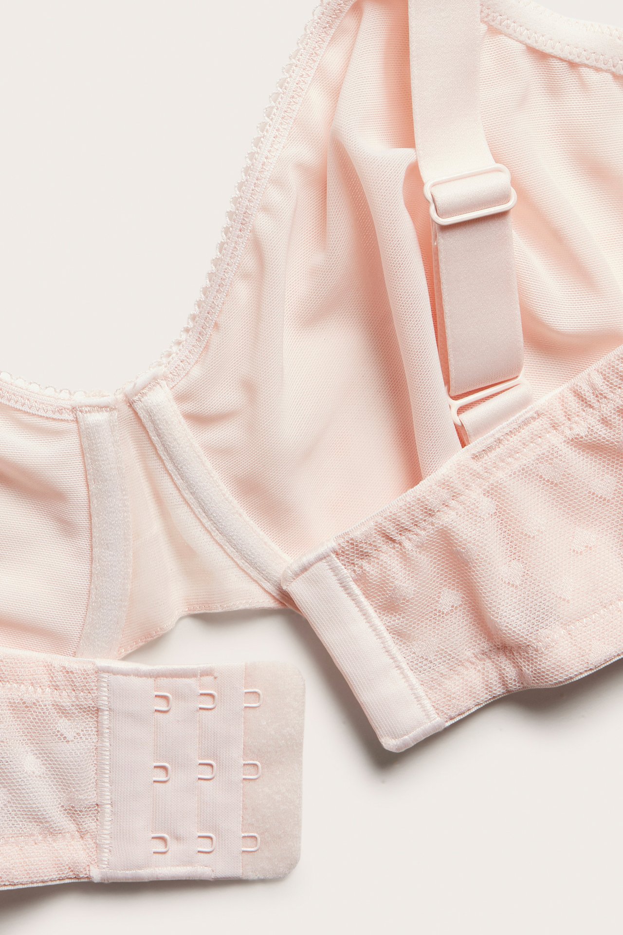 Nærbilde av en lyserosa bøyle-BH med diskret hjertemønster og hektefeste.