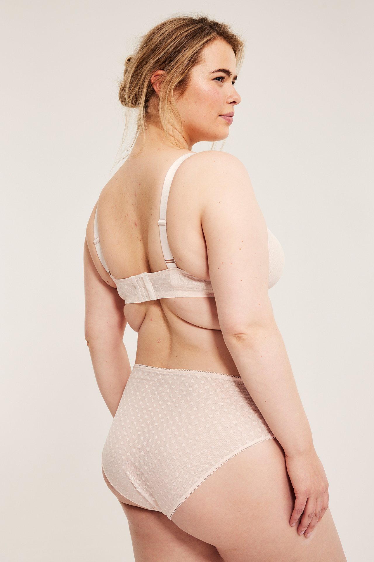 Sido/bakifrån på kvinna i ljusrosa hjärtmönstrade briefs i mesh med picotkant och matchande behå.