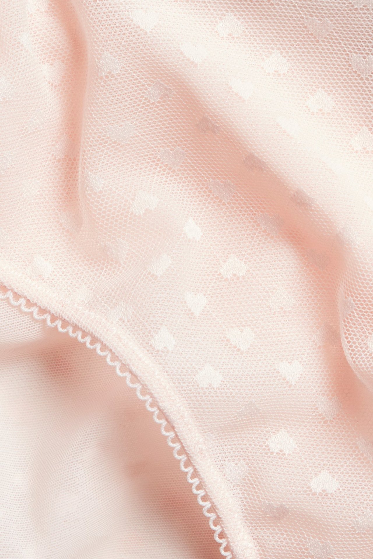 Nærbilde av lys rosa mesh-truser med hvitt hjertemønster og picotkant.