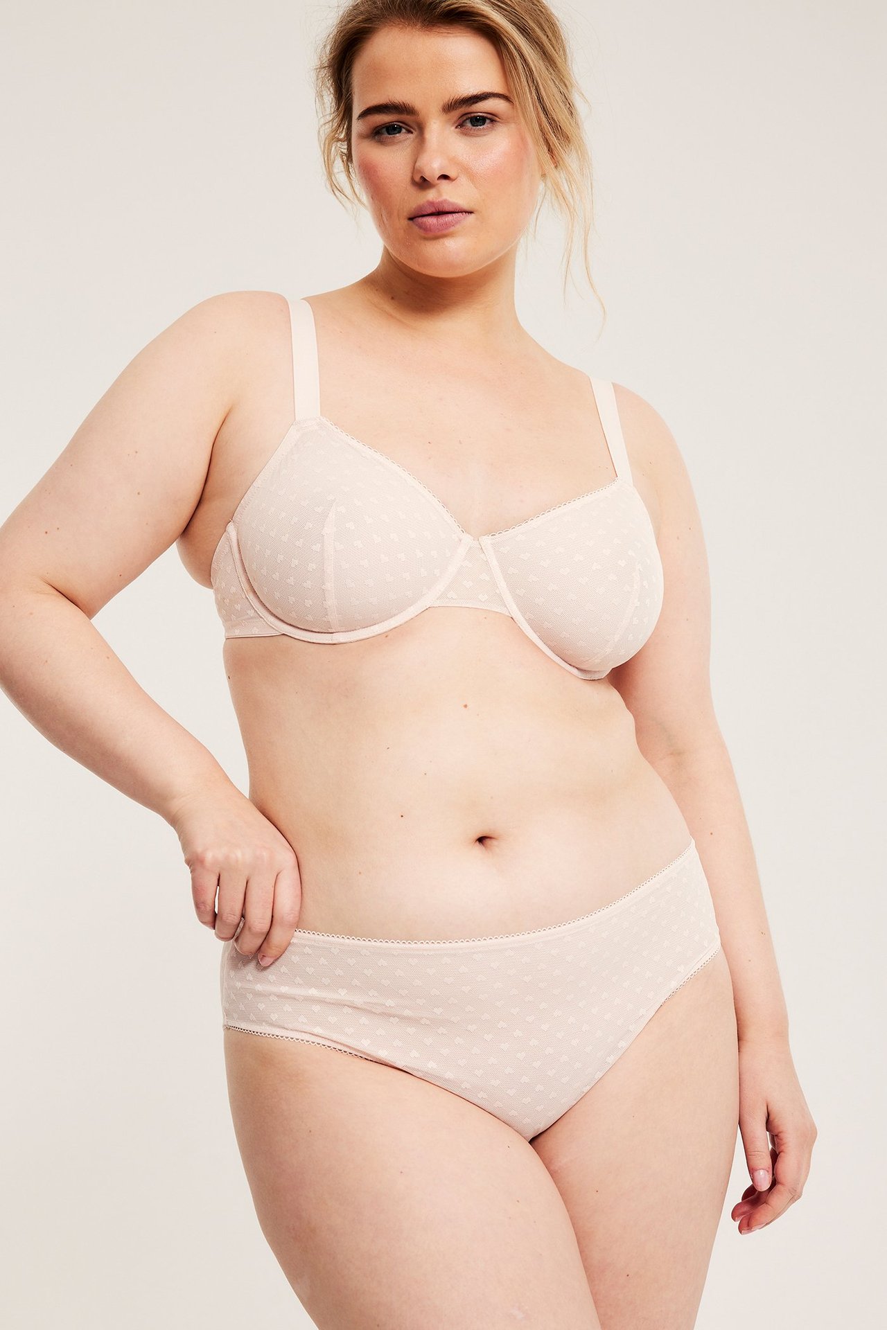 Widok z przodu, kobieta w jasnoróżowych figach z siateczki w serduszka i pasującym staniku.