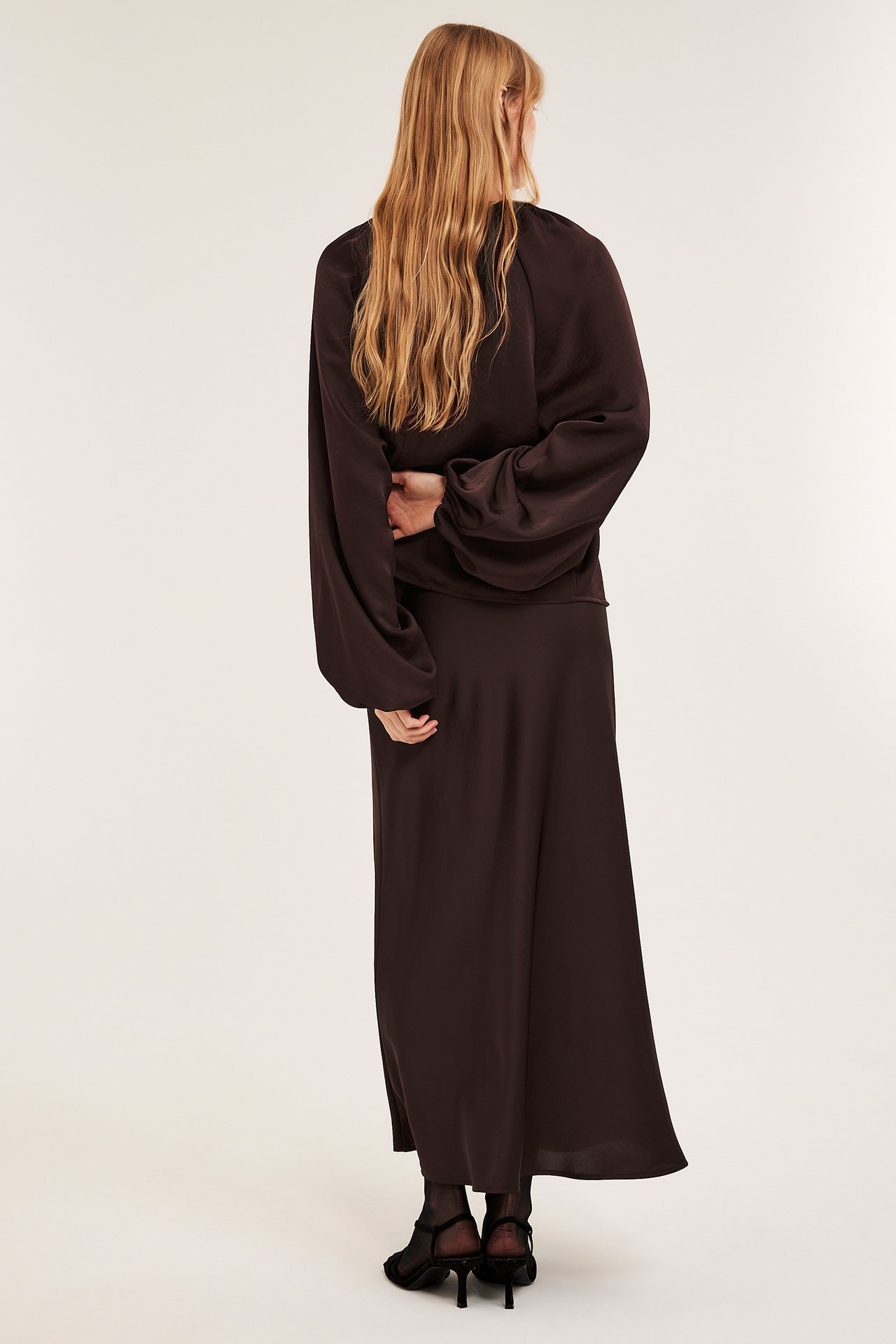 Naisen selkäkuva: viininpunainen pusero volyymihihoilla, yhteensopiva hame ja mustat korkokengät.