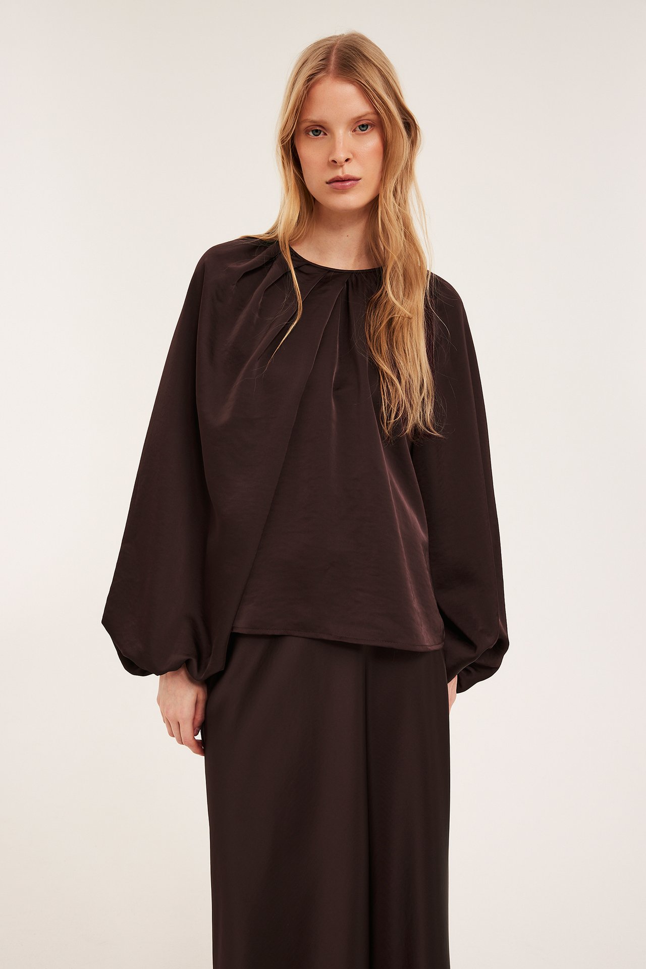 Edestä: Nainen löysässä viininpunaisessa polyesteripuserossa, rypytetty pääntie ja pallohihat.