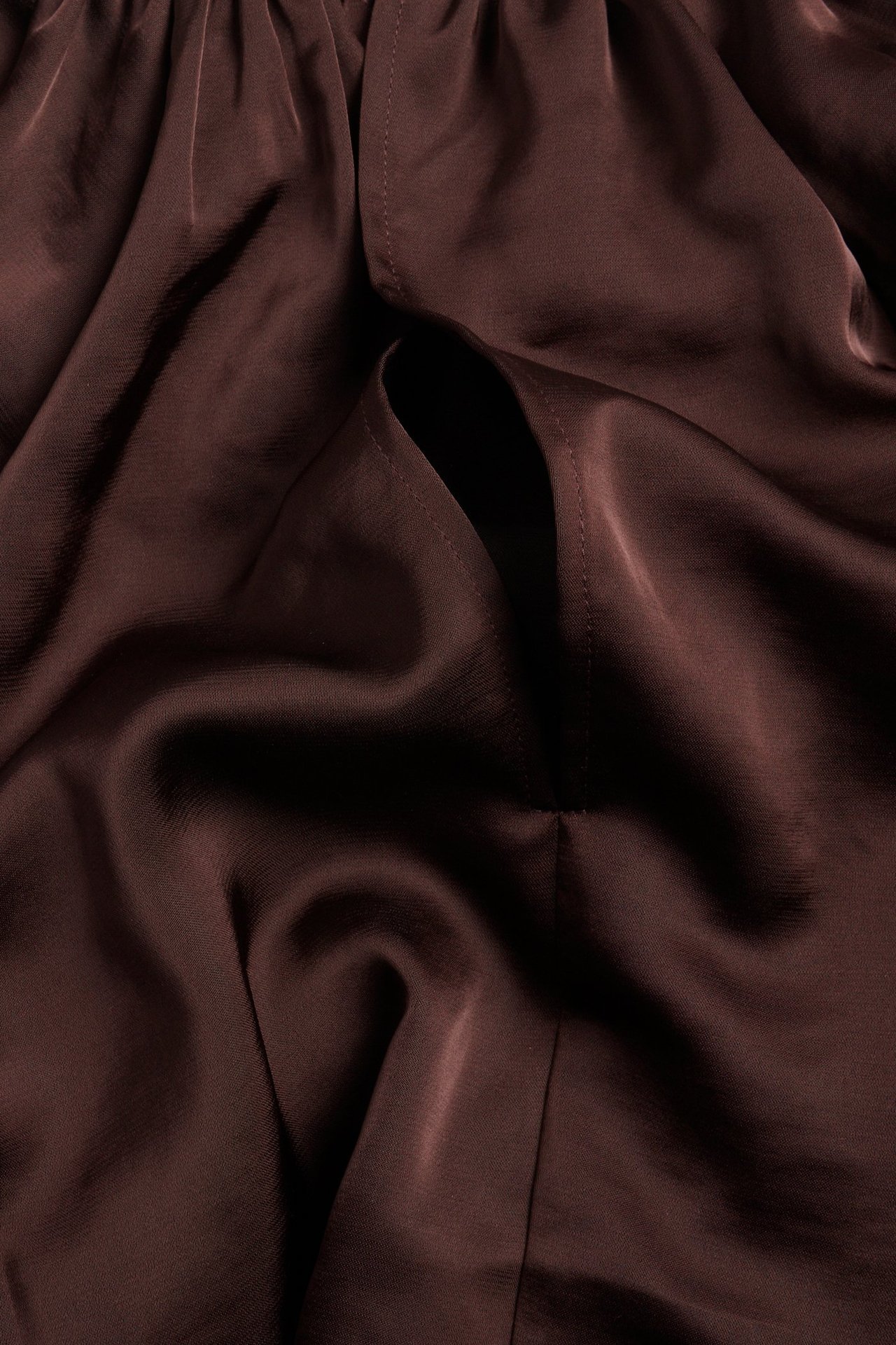 Zbliżenie na bordowy poliestrowy materiał bluzki, ukazujące miękkie fałdy i szyty detal przypominający kieszeń.