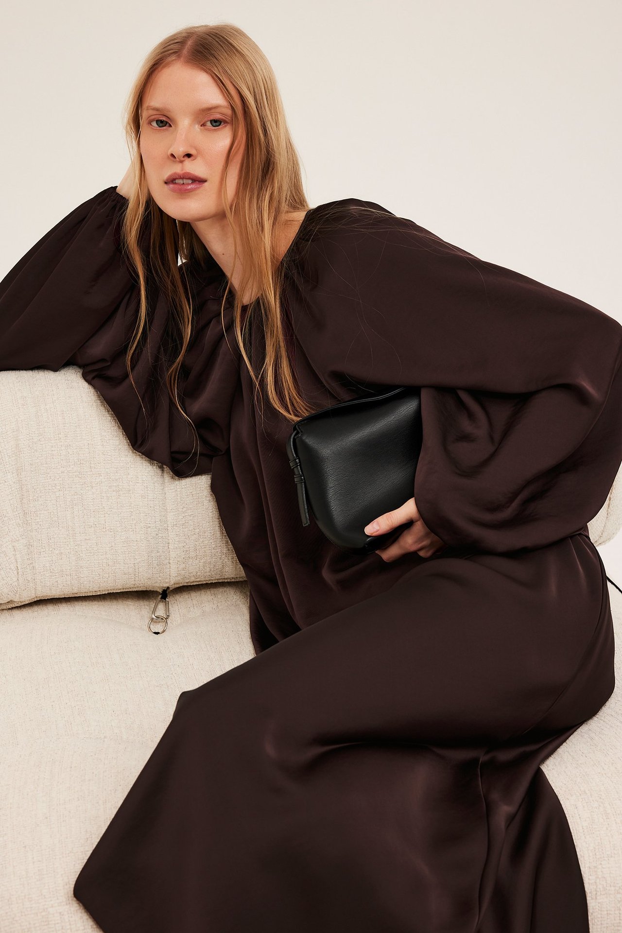 Framifrån: kvinna i lös vinröd polyesterblus med voluminösa ärmar, håller en svart handväska.