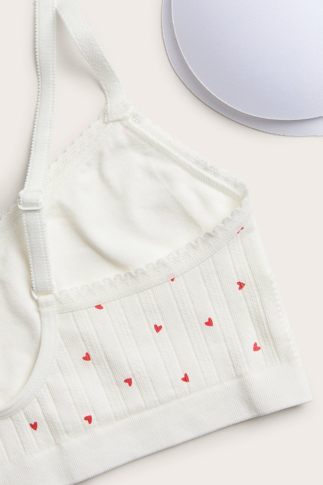 Zbliżenie na kremowy biustonosz bezszwowy z czerwonym wzorem serc i koronką, z dwoma wkładkami.