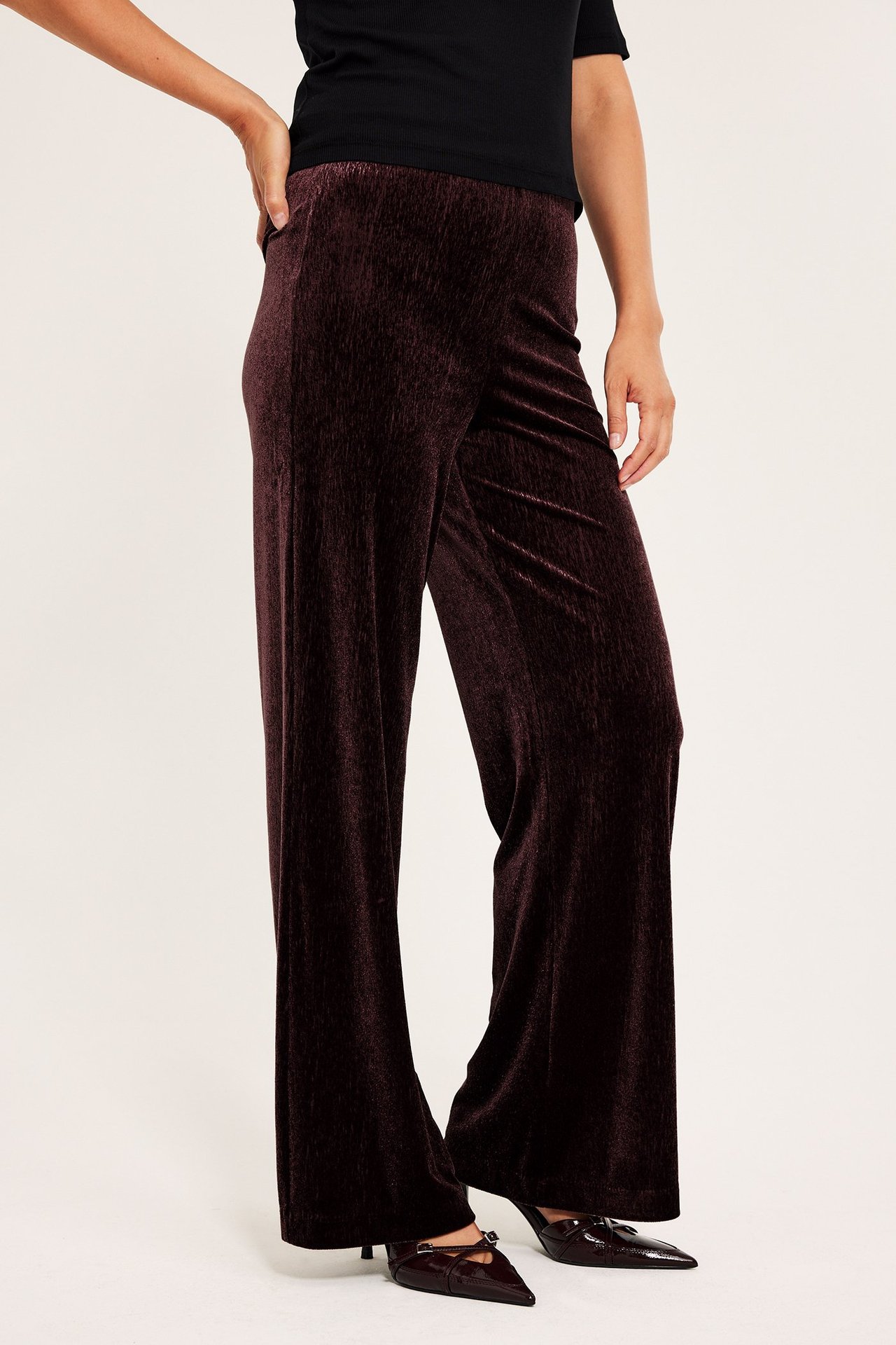Kvinnelig modell har vinrøde velour bukser med vide ben, frontvisning.
