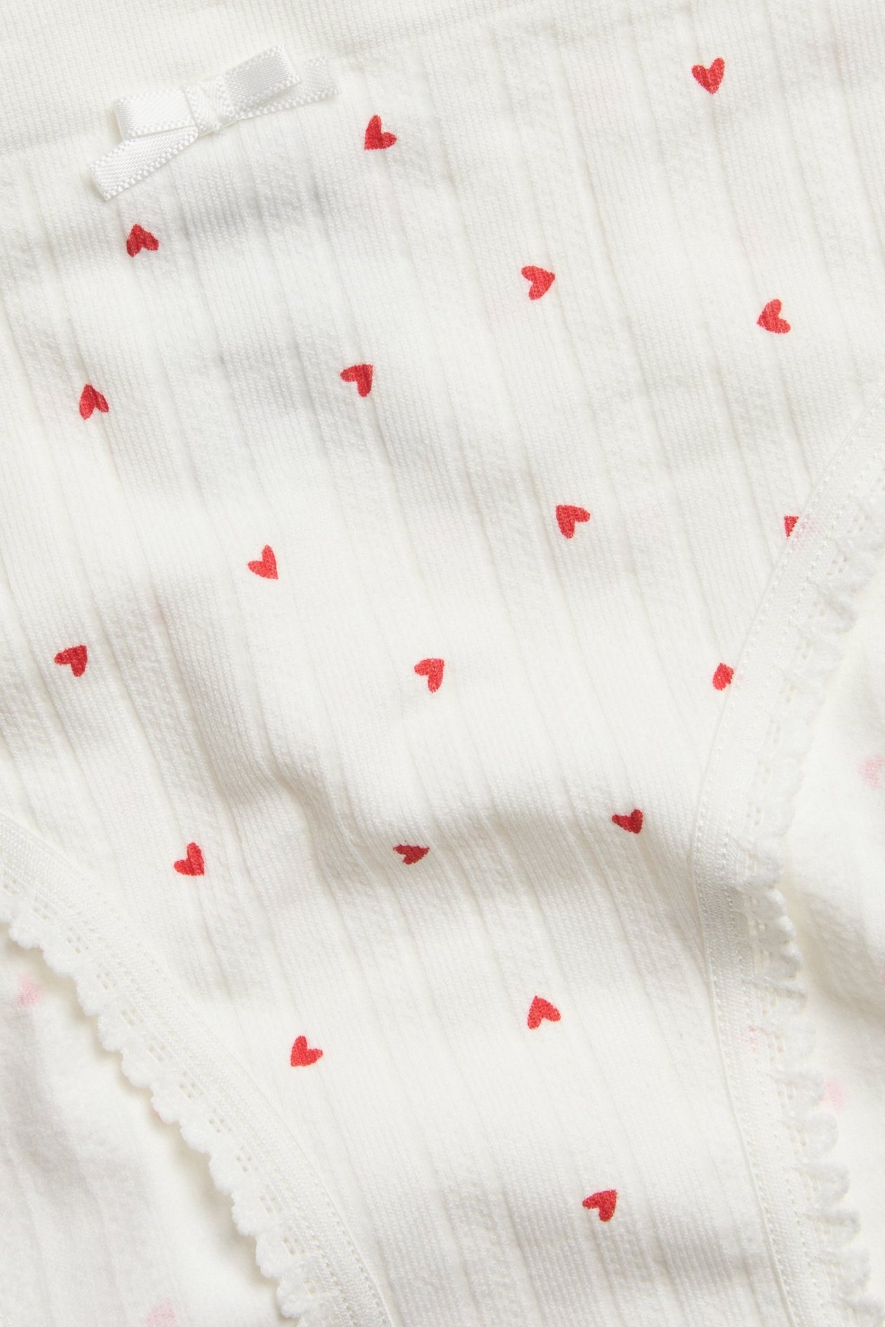 Zbliżenie na bezszwowe figi brief ecru z czerwonym wzorem serc, prążkowaną dzianiną i kokardką.