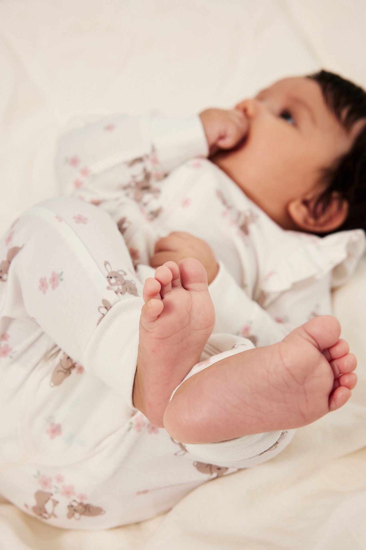 Frontalvisning av en baby i offwhite pyjamas med rysjer, kanin- og blomstermønster.