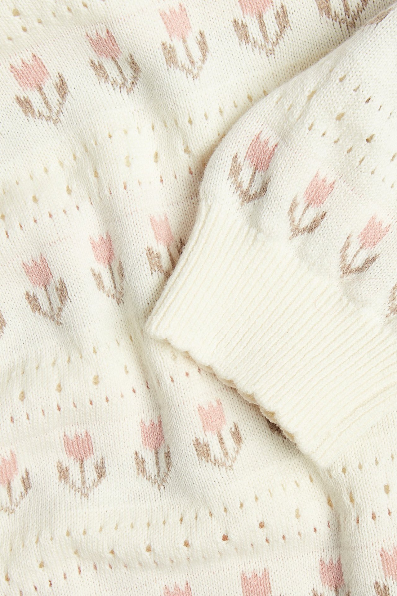 Zbliżenie na ecru bawełniany sweter żakardowy z różowym kwiatowym wzorem i ściągaczem.