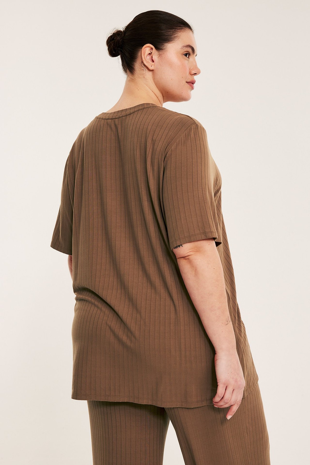 Ryggvy av en kvinna i en lång, lös brun ribbad t-shirt och matchande ribbade byxor.