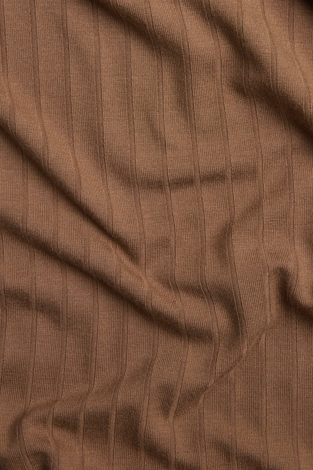 Närbild av brunt ribbat t-shirt-tyg, visar dess vertikala struktur och mjuka veck.