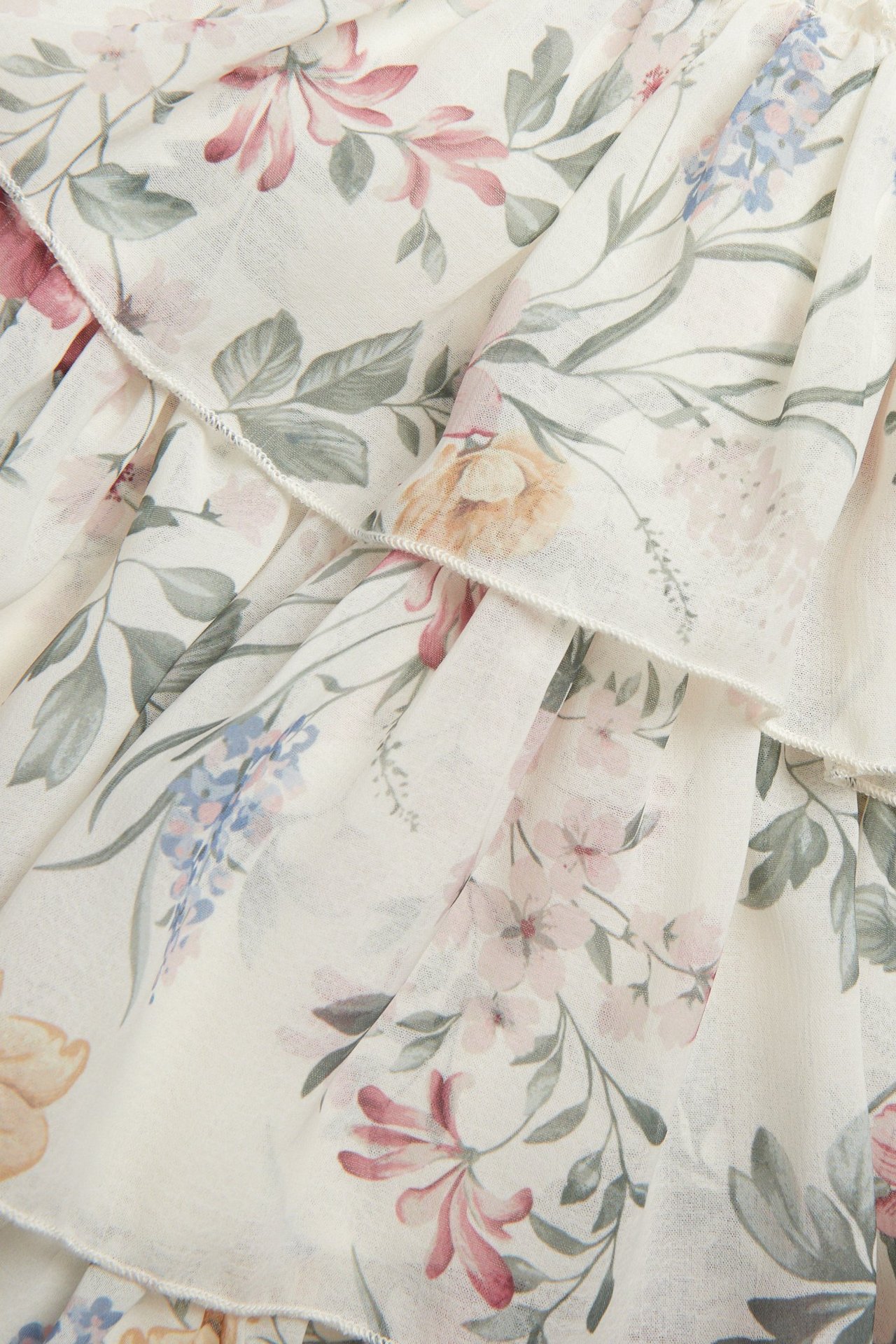 Nærbilde av en offwhite blomstret chiffonkjole som viser volanger og et fargerikt trykk.