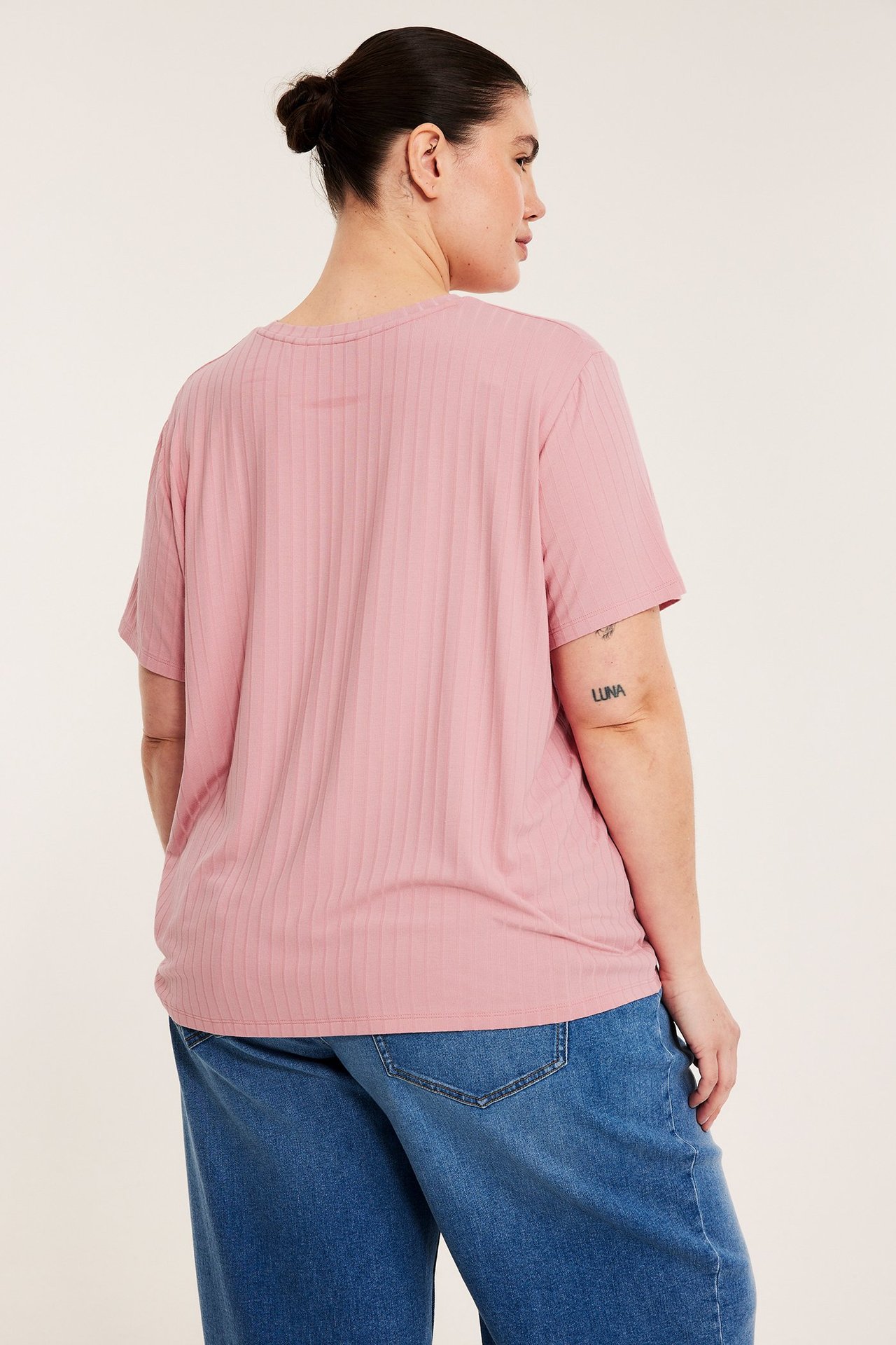 Bakifrån, kvinna i avslappnad passform rosa ribbad t-shirt och blå vida jeans.
