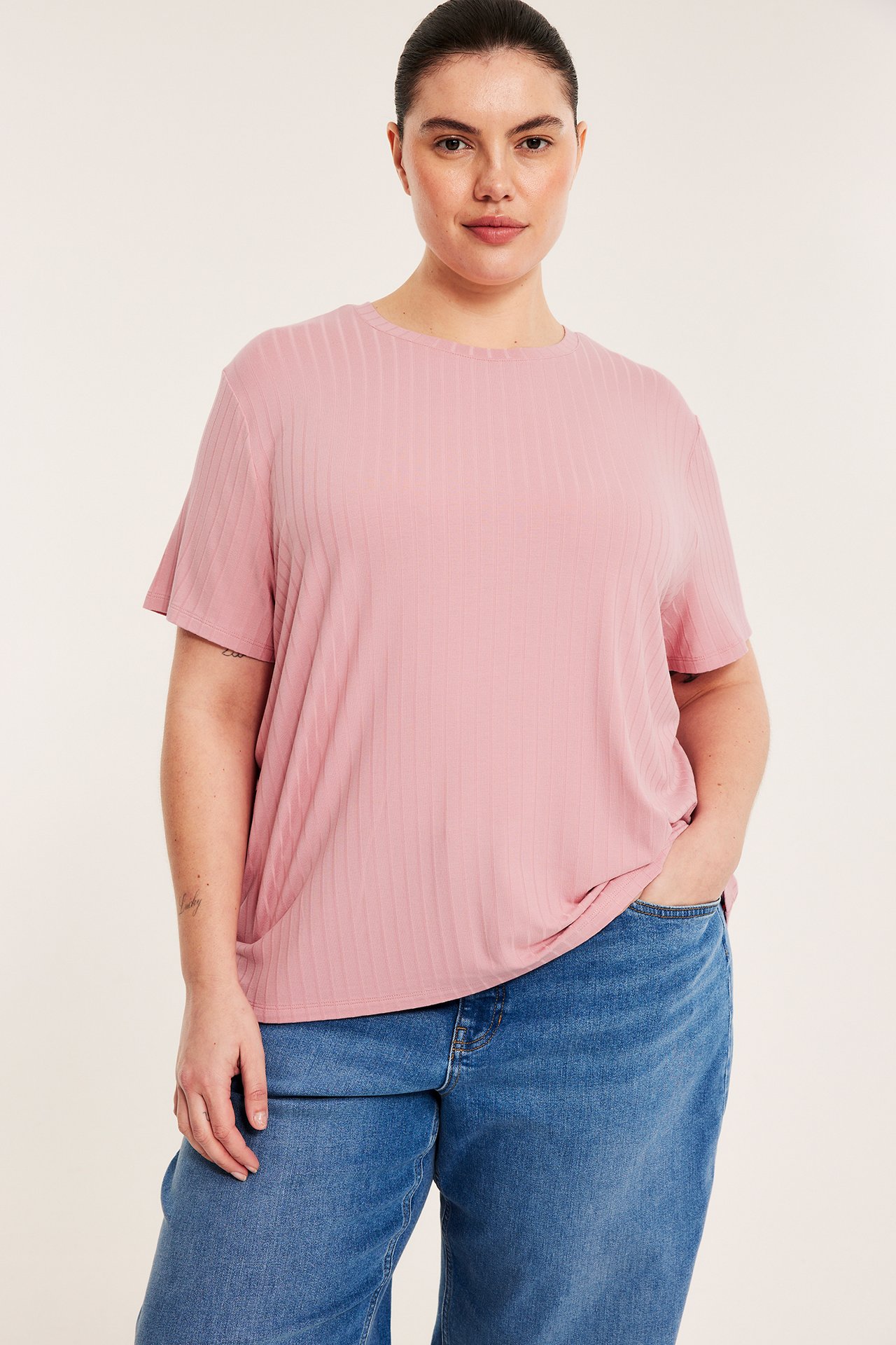 Framsida på kvinna i rosa ribbad t-shirt med boxig passform, korta ärmar och blå löst sittande jeans.