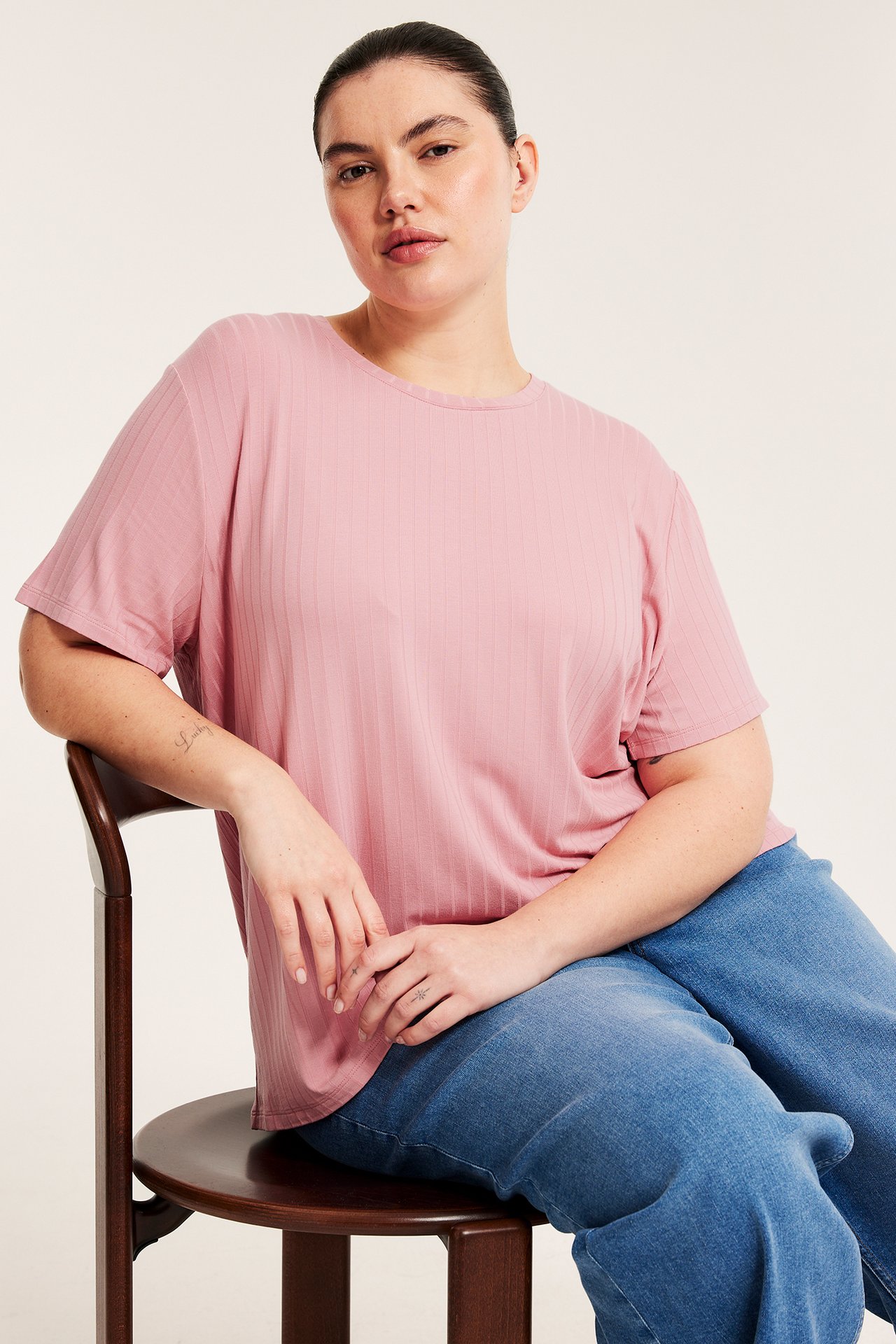 Framifrån: kvinna i en boxig rosa ribbad t-shirt och lösa blå jeans.