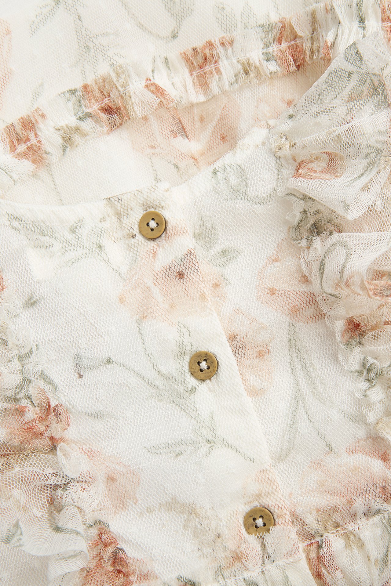 Zbliżenie na ecru siatkową sukienkę w kwiaty z kropkowaną strukturą, falbankami i drewnianymi guzikami.
