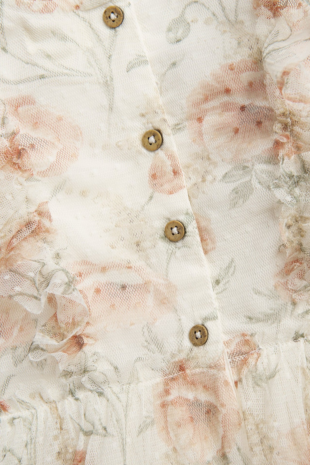 Zbliżenie: kremowa kwiecista sukienka z siateczki, kropki, falbanka i brązowe guziki.
