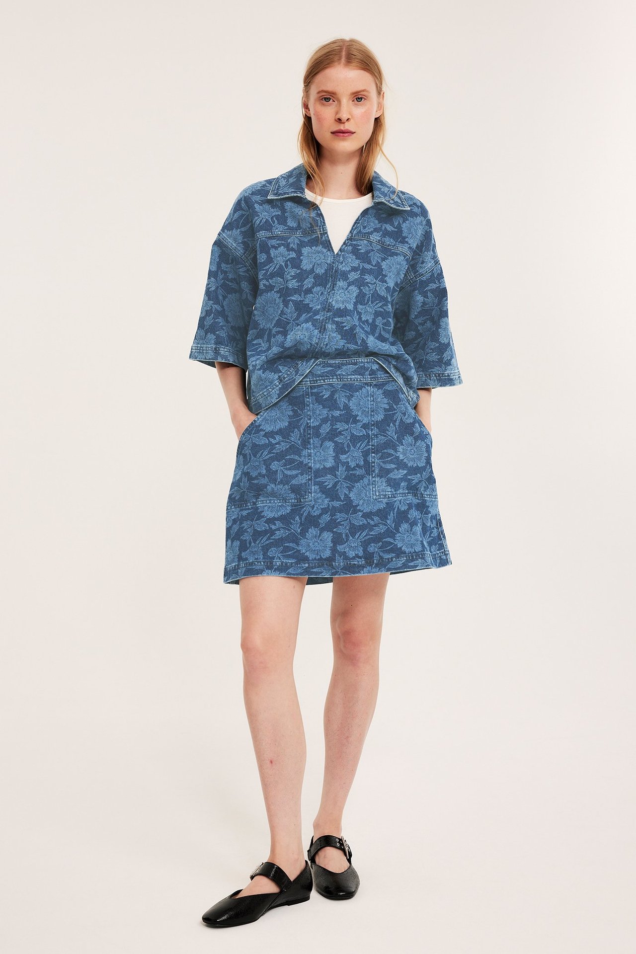 Blått blomstret denim miniskjørt med frontlommer, matchende denimskjorte, hvit topp og svarte flate sko.