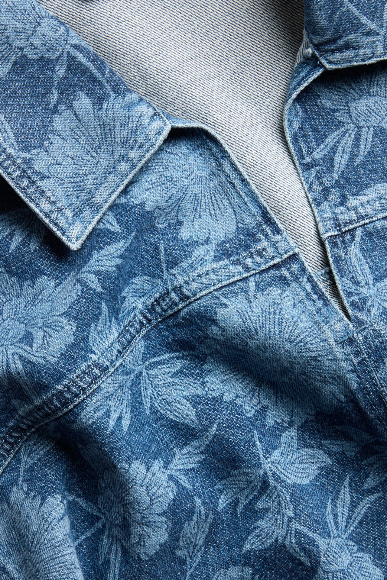 Zbliżenie niebieskiej koszuli jeansowej z kwiatowym wzorem i kołnierzem w serek.