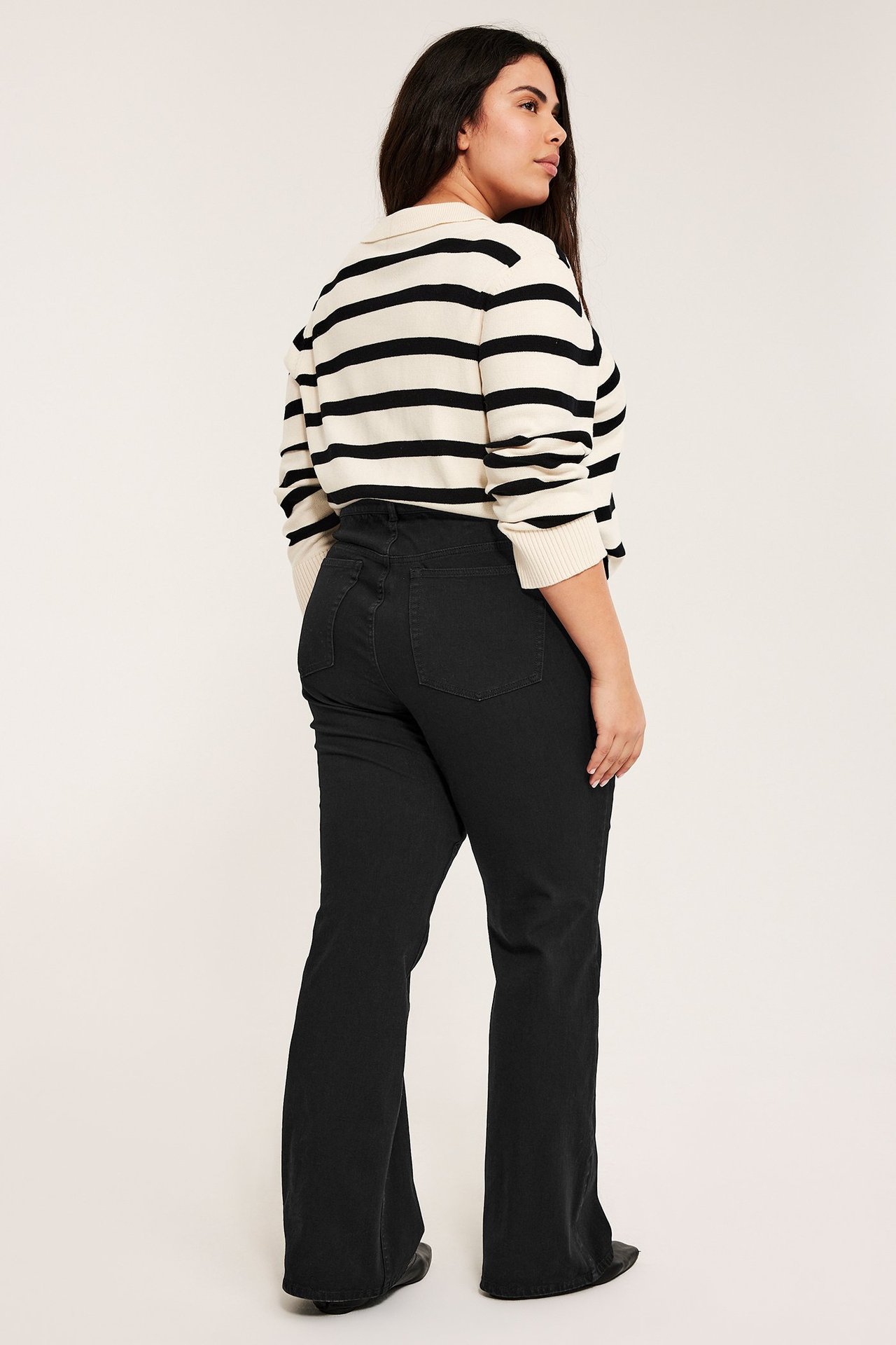 Sned bakifrån-vy av en kvinna i svarta höga bootcut-jeans och en krämvit- och svartrandig långärmad tröja.