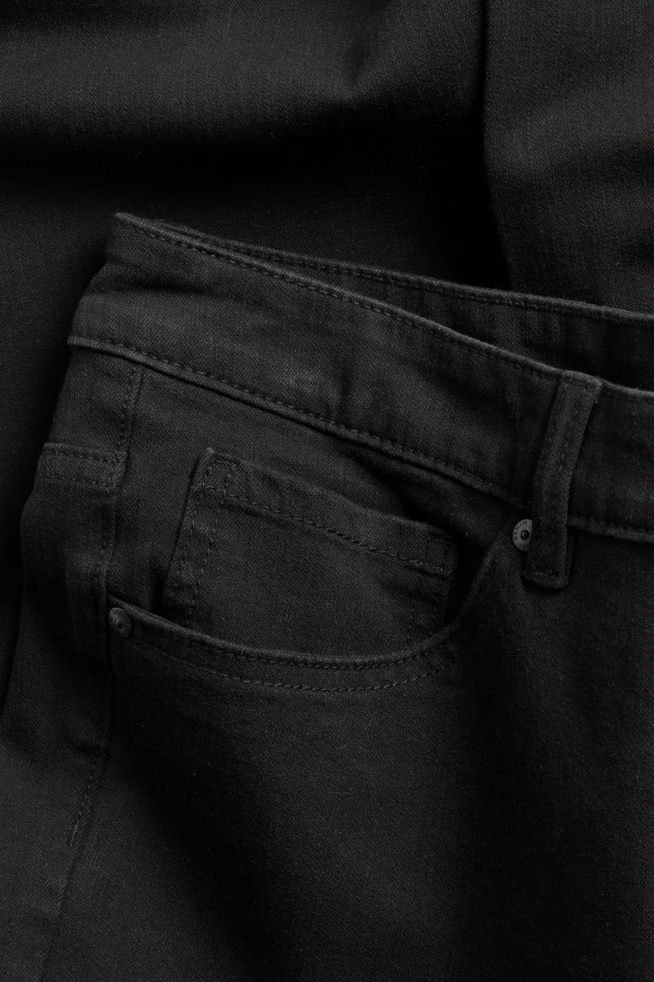 Lähikuva mustista korkeavyötäröisistä bootcut-farkuista, etutaskun ja vyötärön yksityiskohdat näkyvillä.