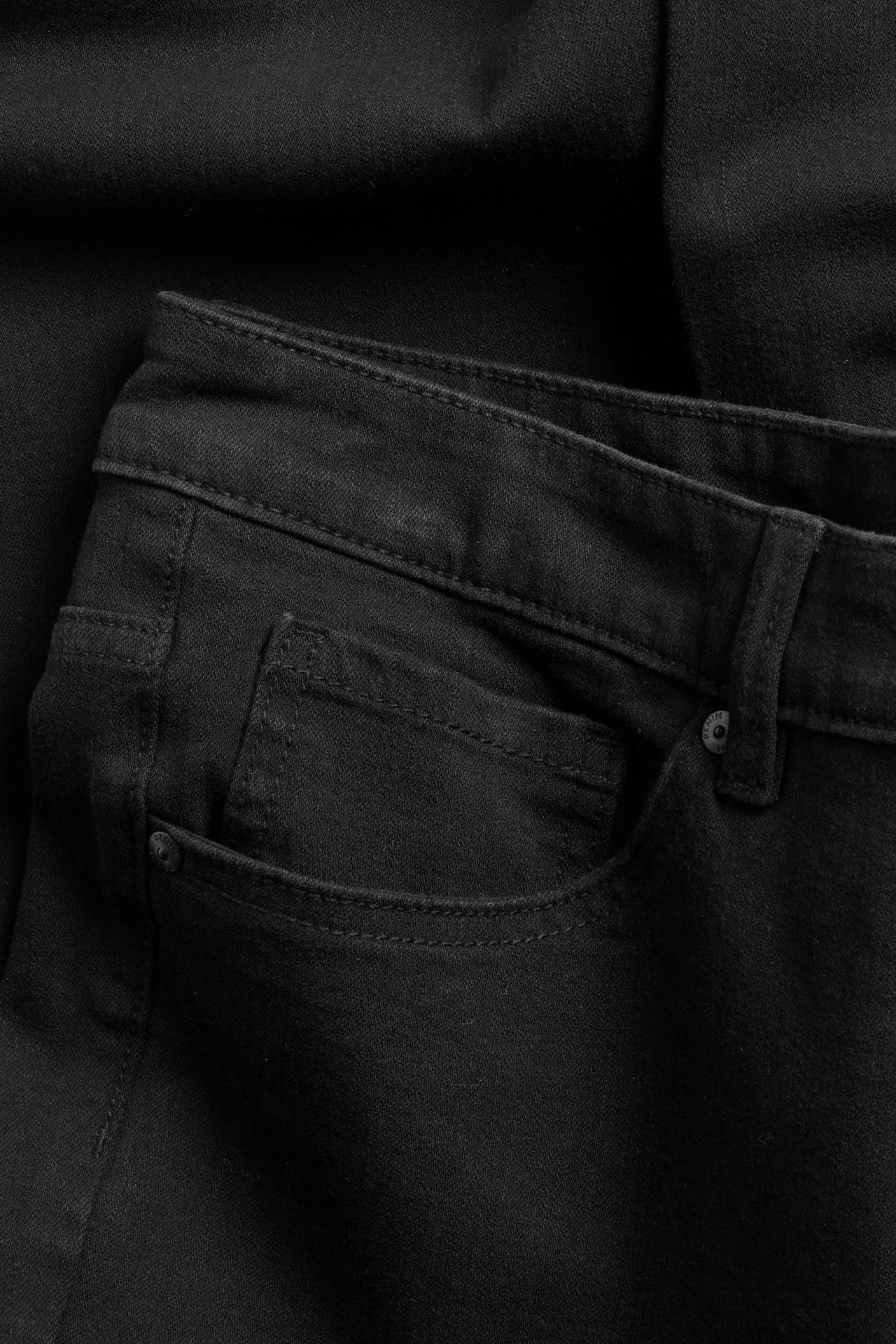 Zbliżenie na czarne jeansy bootcut z wysokim stanem, pokazujące przednią kieszeń i pasek.