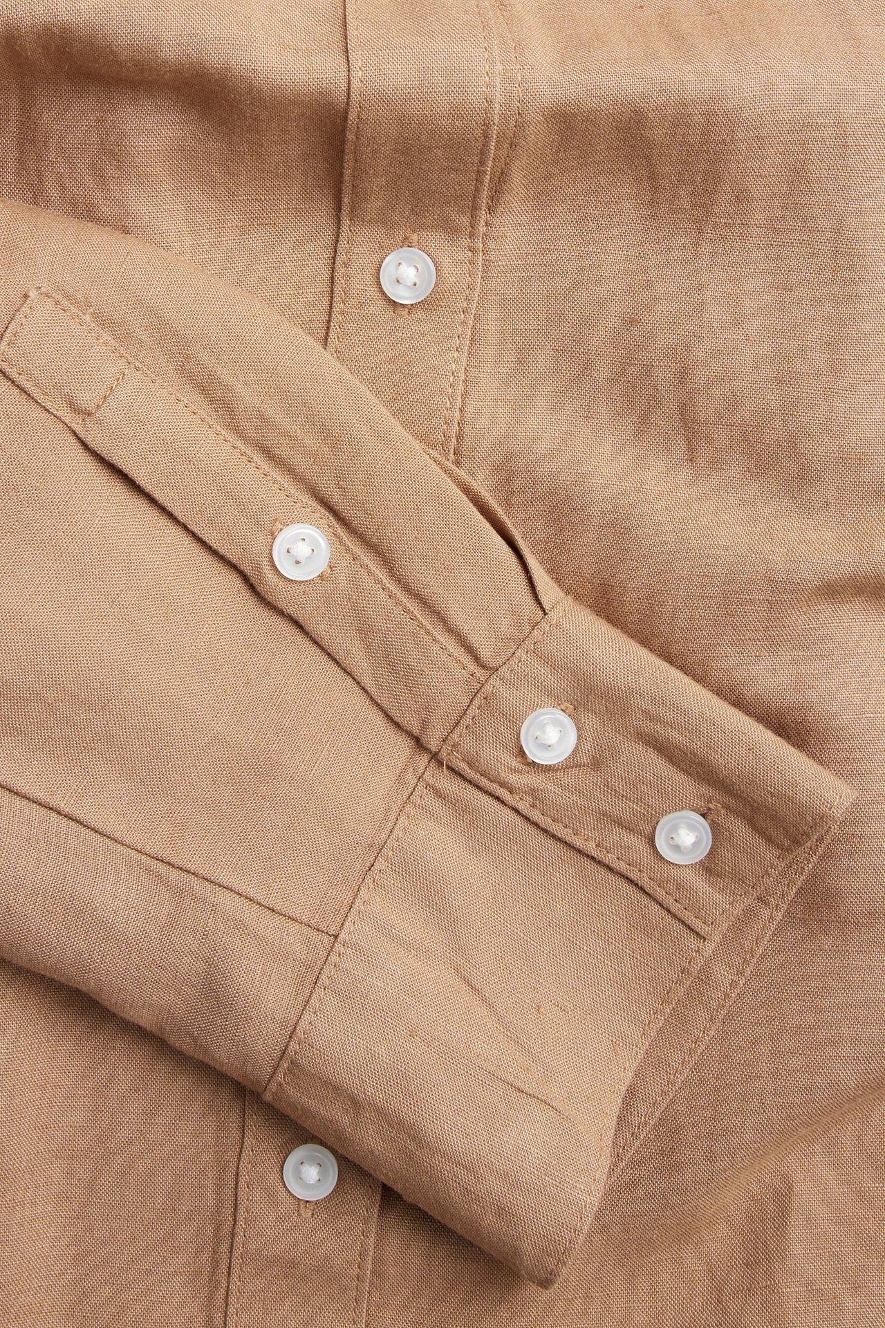 Närbild av en beige linneblandningsskjorta, som visar ärmmanschetten och vita knappar.