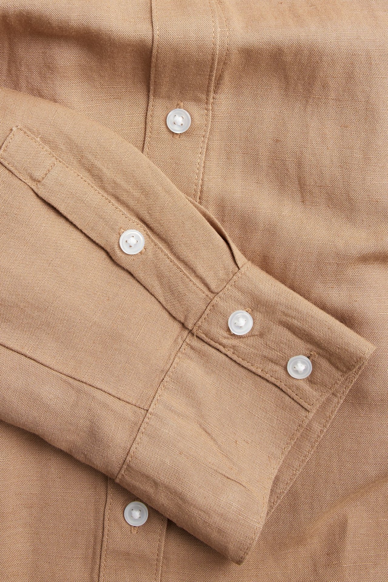 Zbliżenie na beżową koszulę z mieszanki lnu, pokazujące mankiet rękawa i białe guziki.