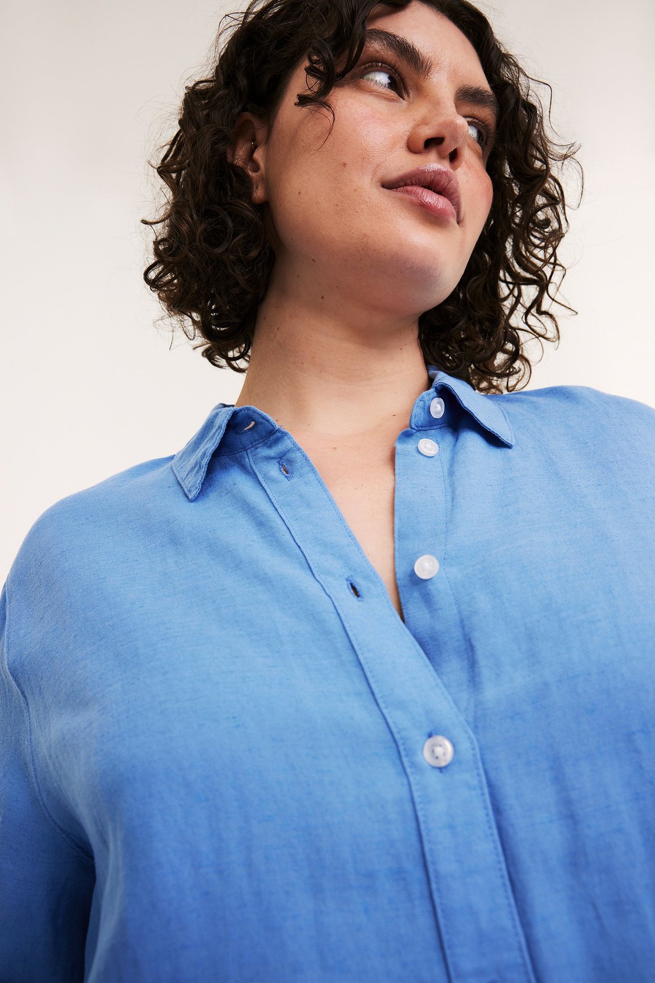 Närbild på en kvinna i en blå skjorta i linnemix med vita knappar.