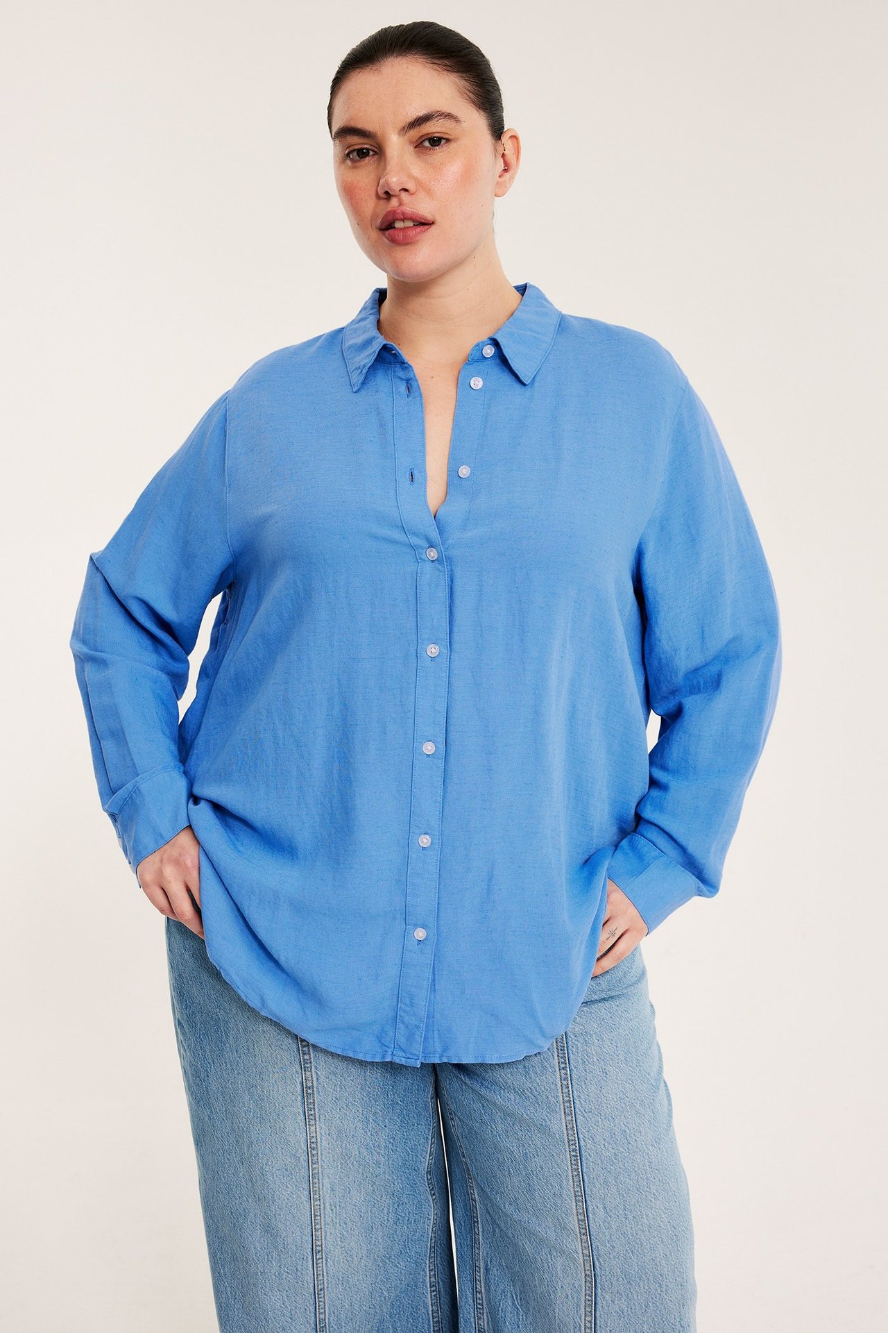Framifrån, kvinna i blå linneblandningsskjorta med knappar och ljusblå vida jeans.