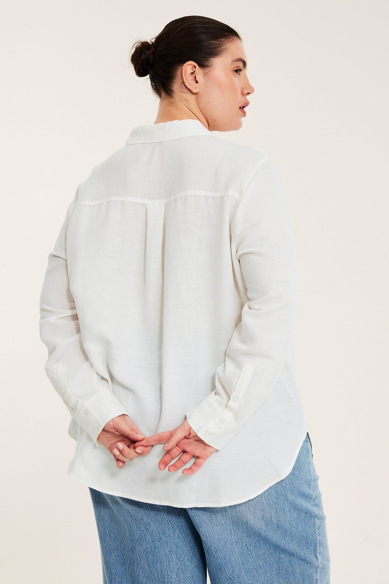 Ryggvy av en kvinna i en vit linneblus med långa ärmar och ljusblå jeans.